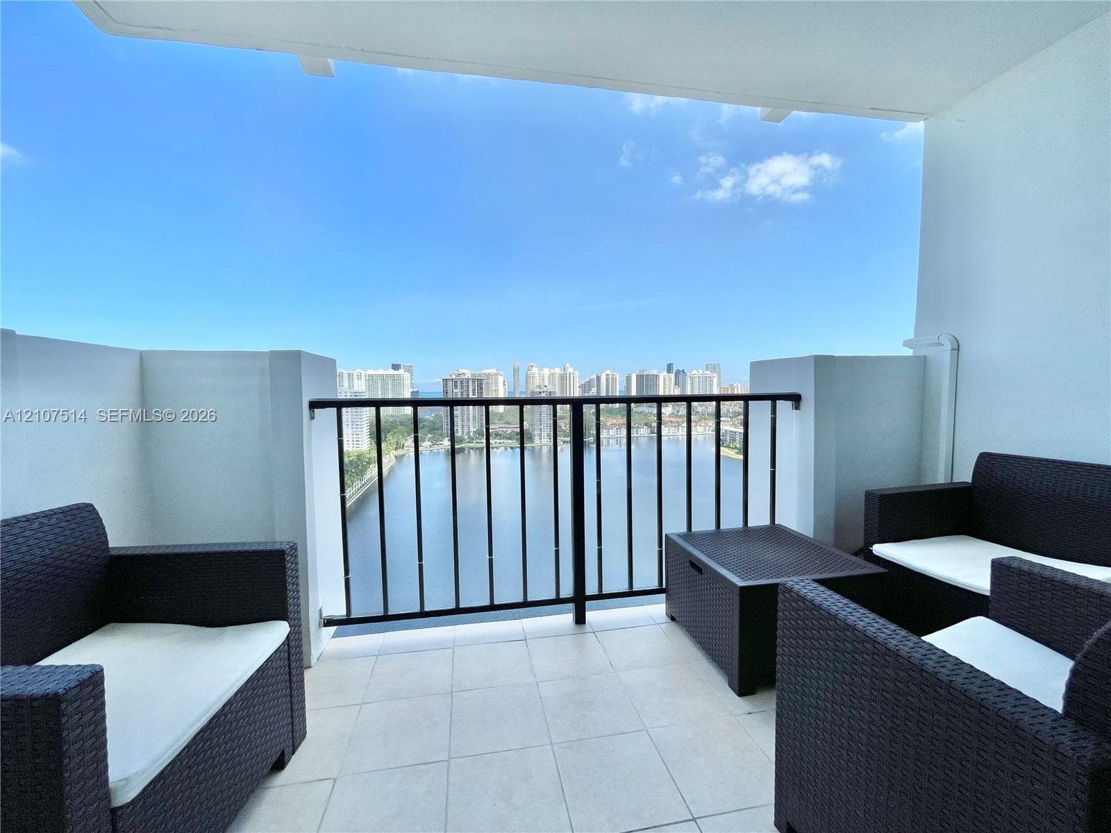 Private balcony featuring light-toned tile flooring and black metal railing, overlooking the water and surrounding city skyline