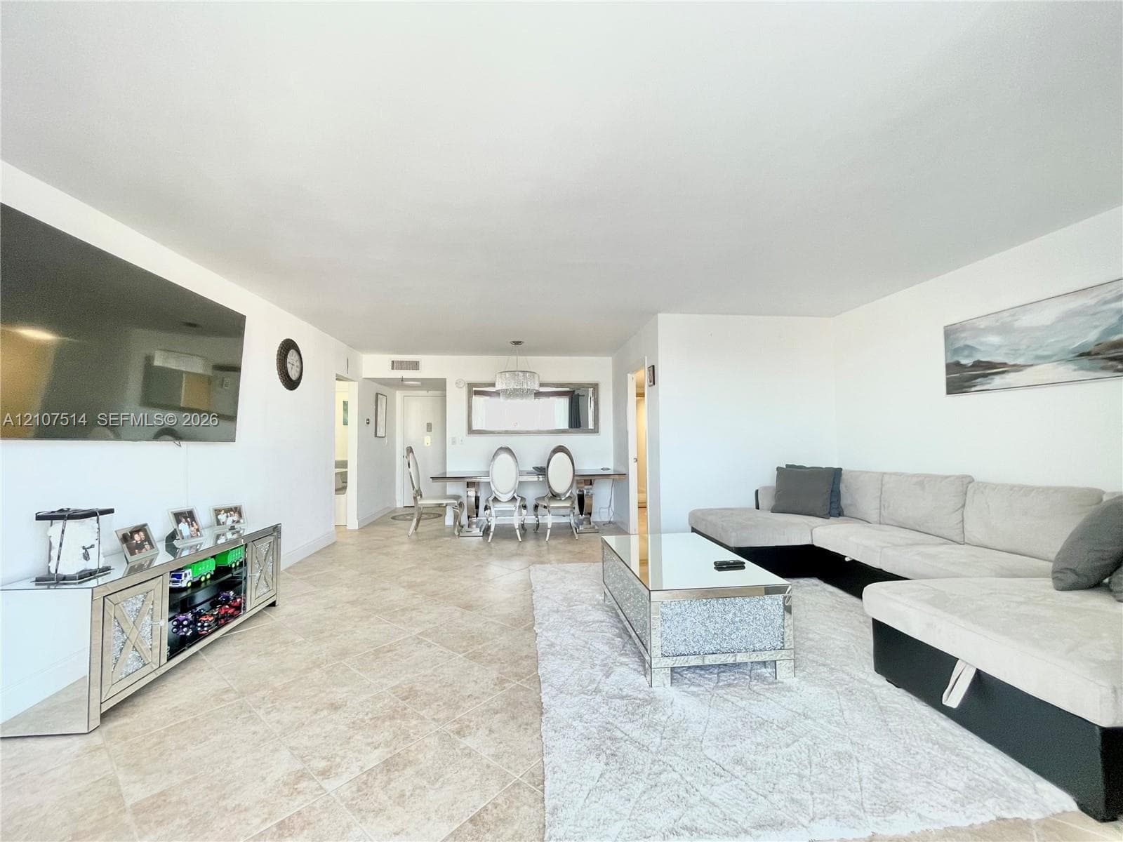 Open-concept living space featuring large-format ceramic tile flooring, neutral wall finishes, and a contemporary multi-light chandelier