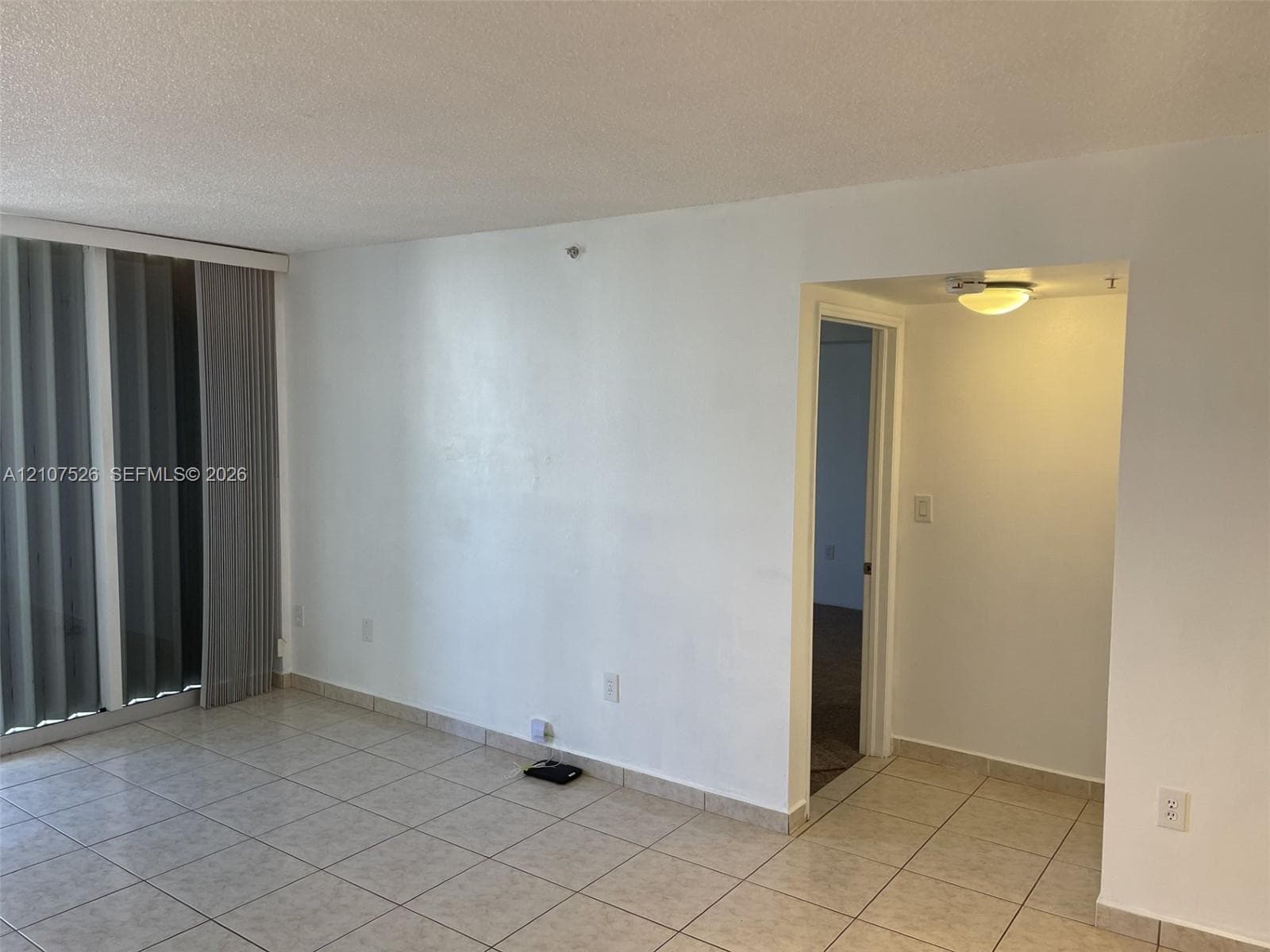 Interior space featuring neutral tile flooring, vertical window blinds, and a flush-mount ceiling light fixture