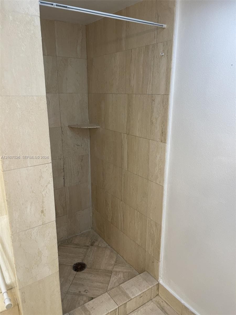 Walk-in shower featuring floor-to-ceiling stone-tile surround, neutral-toned finish, built-in corner shelving, and a tiled shower basin