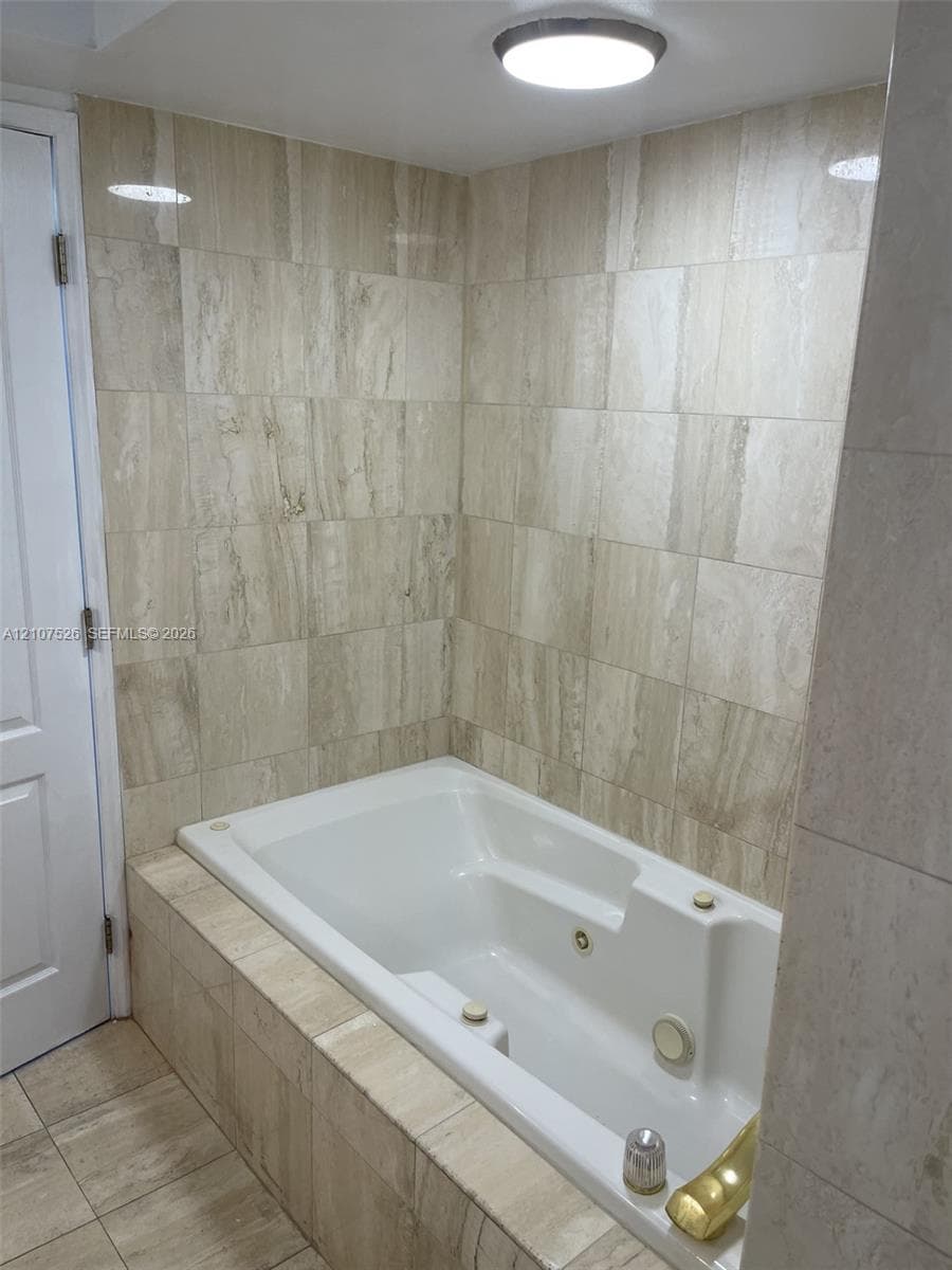 Built-in jetted soaking tub featuring neutral stone-finish tile surround and flooring, flush-mount ceiling lighting, and panel door