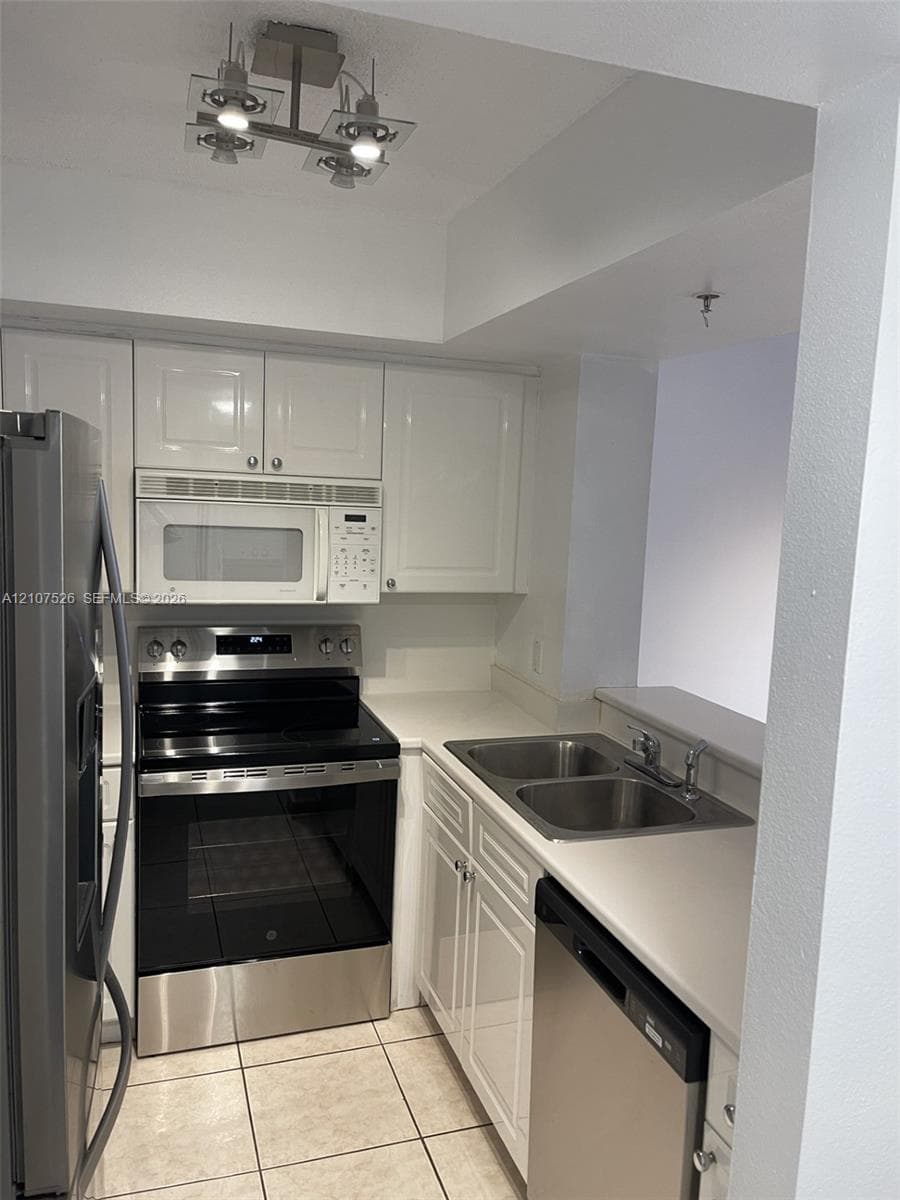 Kitchen featuring white cabinetry, solid-surface countertops, stainless steel appliances, a double-basin undermount sink, and tile flooring