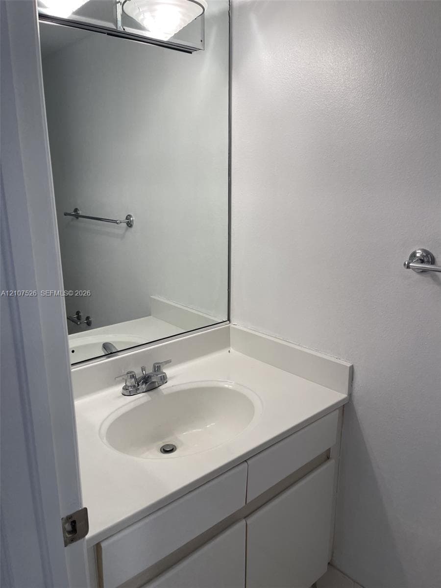 Vanity with integrated sink, solid surface countertop, chrome dual-handle faucet, large wall-mounted mirror, and attached metal hardware