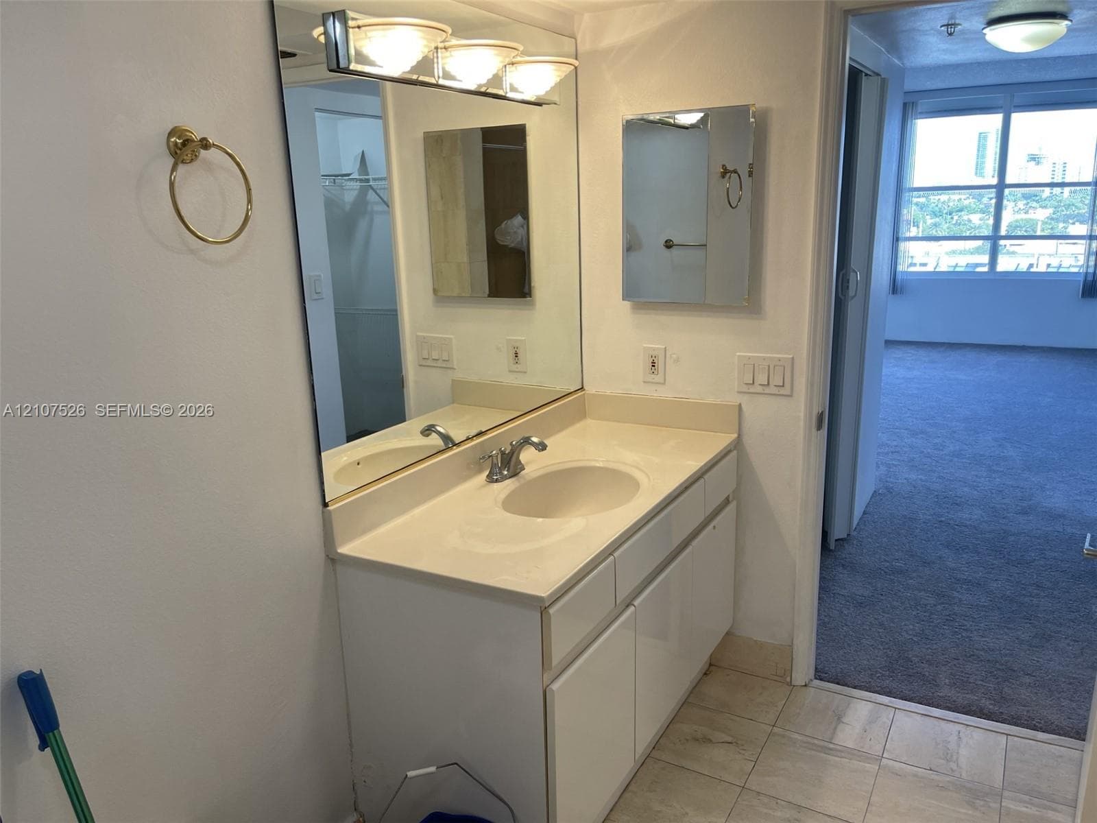 Vanity featuring a solid-surface countertop with an integrated basin, white cabinetry, a large wall-mounted mirror, and triple-bulb vanity lighting