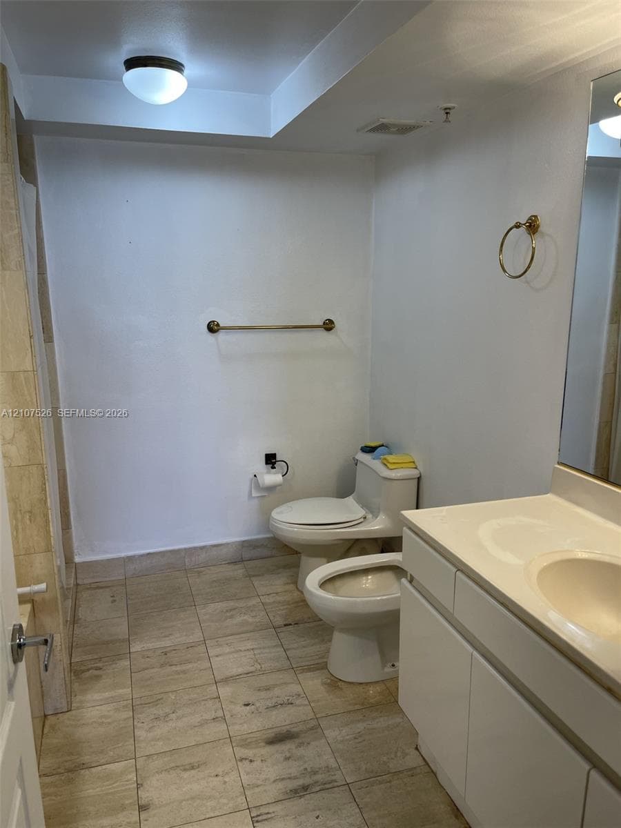 Bathroom featuring a white vanity with an integrated sink, natural stone-finish floor tiling, wall-mounted metallic fixtures, and a glass mirror