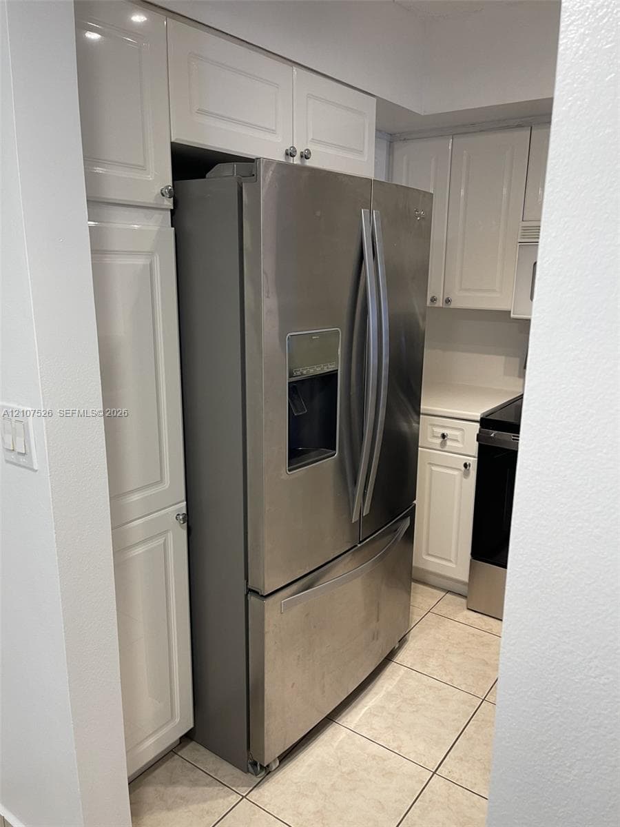 Kitchen featuring white shaker-style cabinetry, stainless steel French-door refrigerator with external water dispenser, and tiled flooring