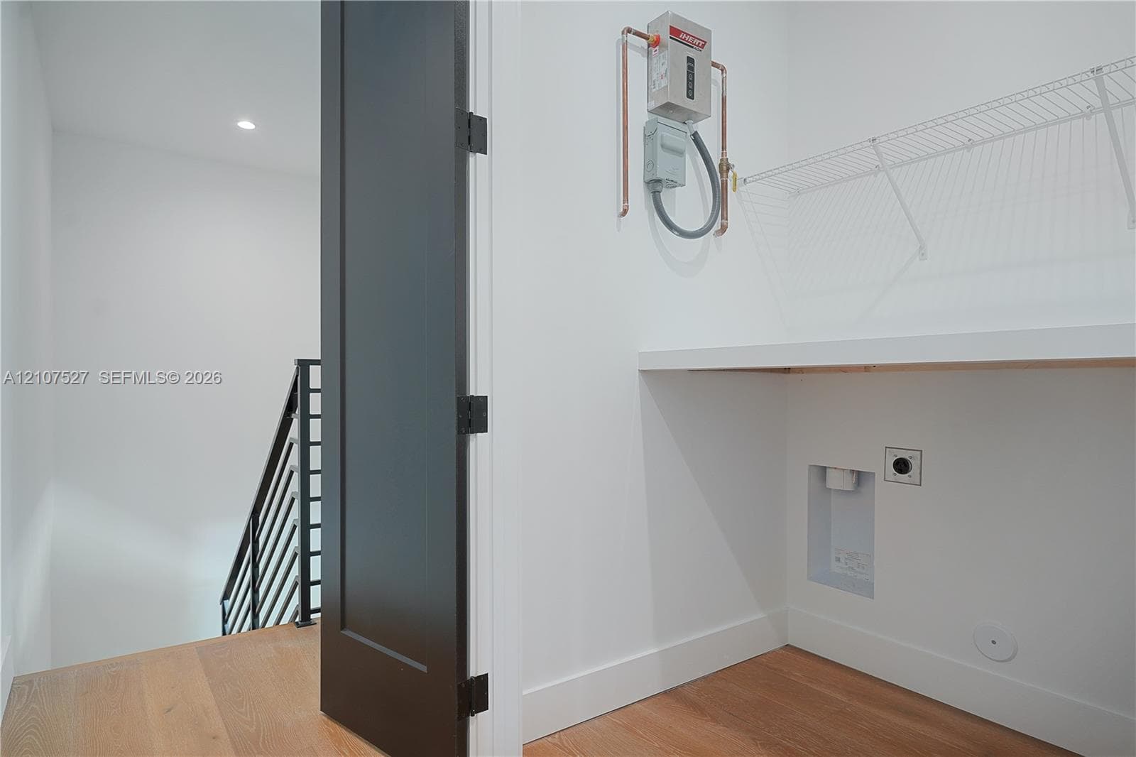 Utility space featuring wood-finish flooring, a wall-mounted tankless water heater, built-in shelving, and a solid-core dark finish interior door
