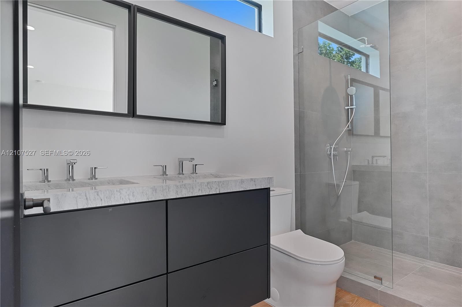 Floating dual-sink vanity with a stone countertop, framed mirrors, glass-enclosed shower with large-format tile, and rectangular transom windows
