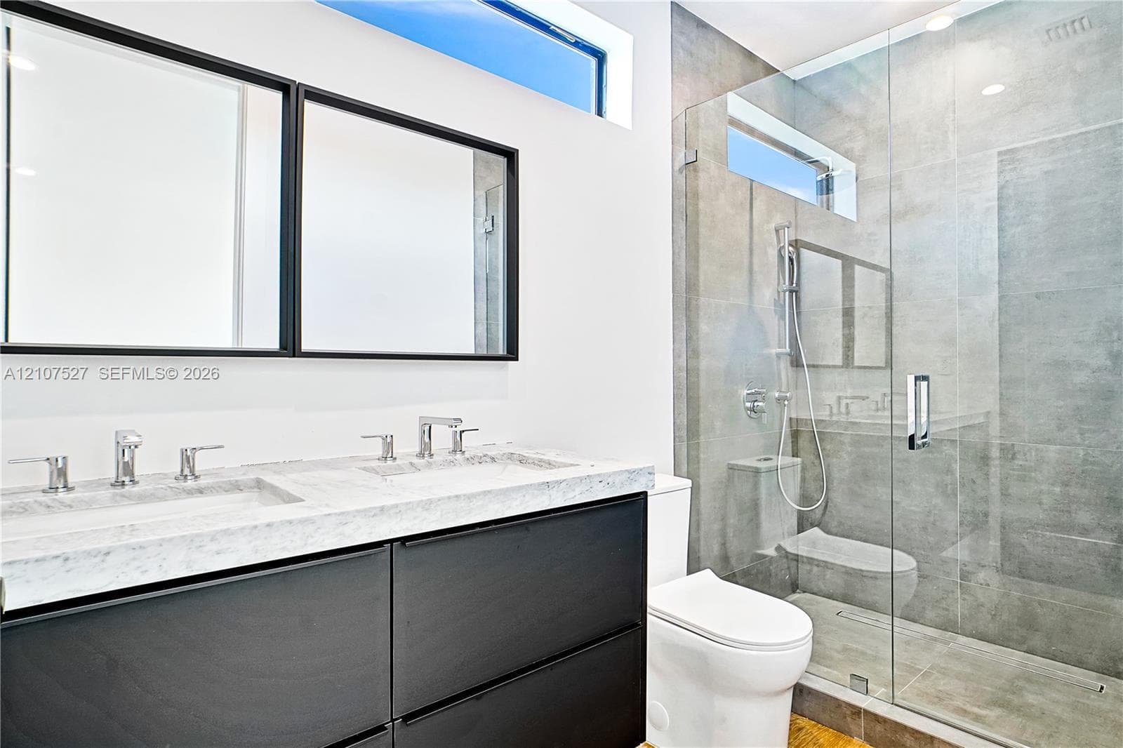 Floating vanity featuring a dual-sink stone countertop, walk-in shower with floor-to-ceiling tile, frameless glass enclosure, and transom windows