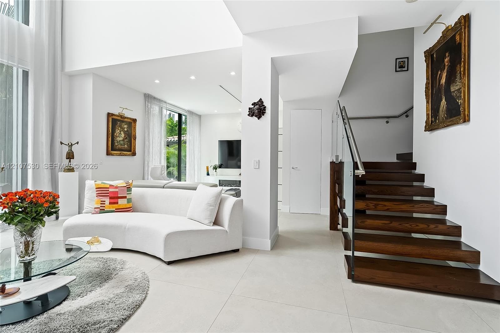 High-ceiling living area featuring large-format tile flooring, a dark wood-tread staircase, and a glass panel railing