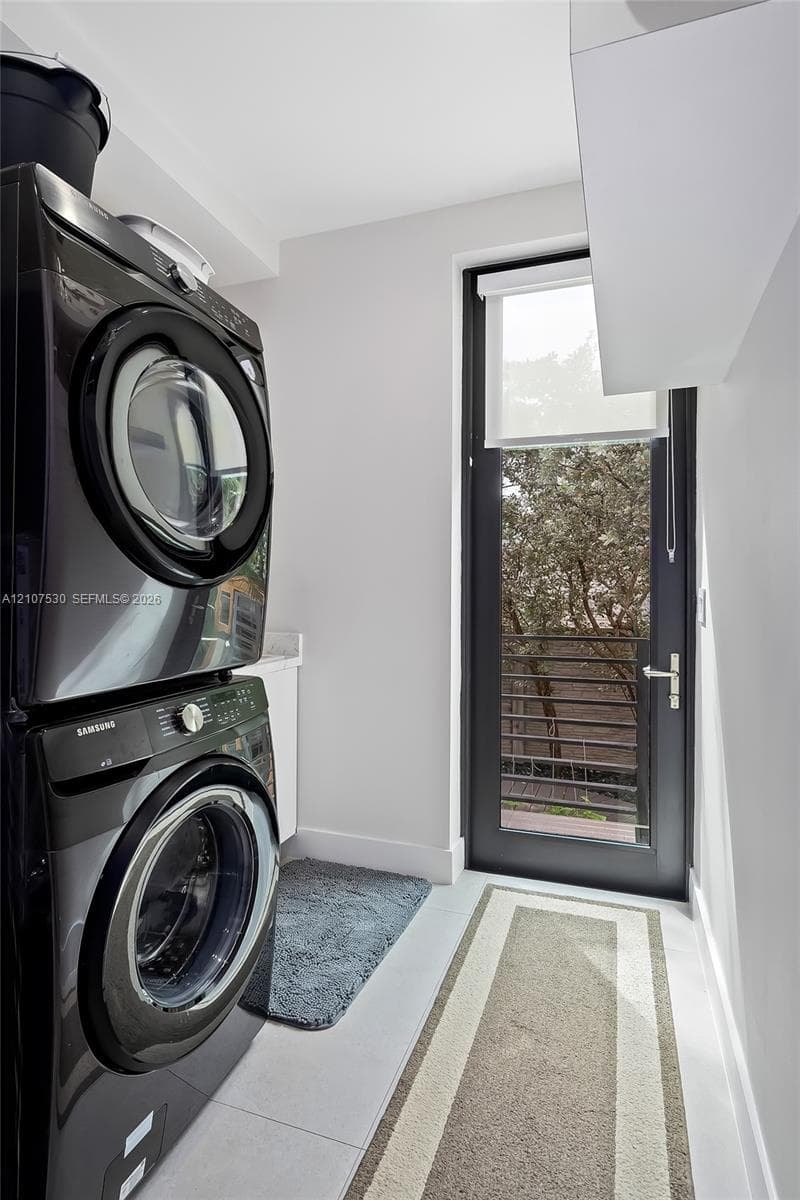 Laundry area featuring stacked appliances, a solid-surface countertop, cabinetry, and a full-height glass-panel door
