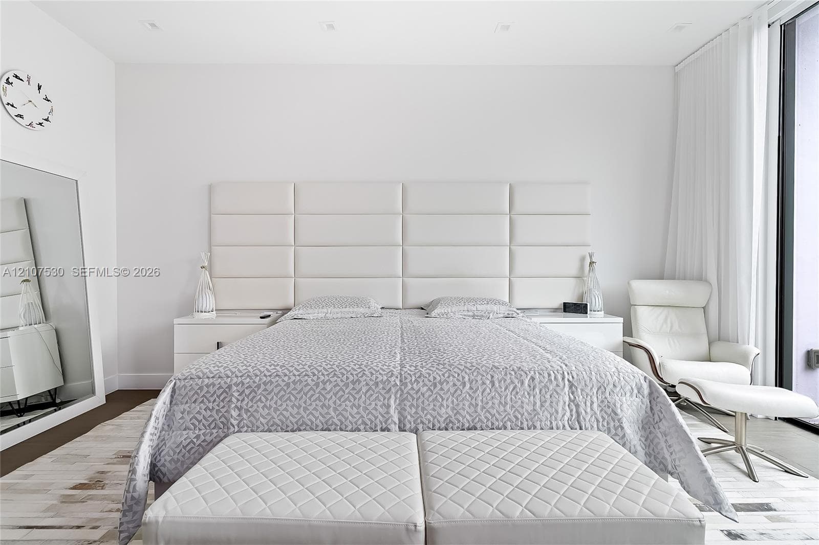Full-height paneled headboard, recessed ceiling lighting, and floor-to-ceiling glass panel with drapery