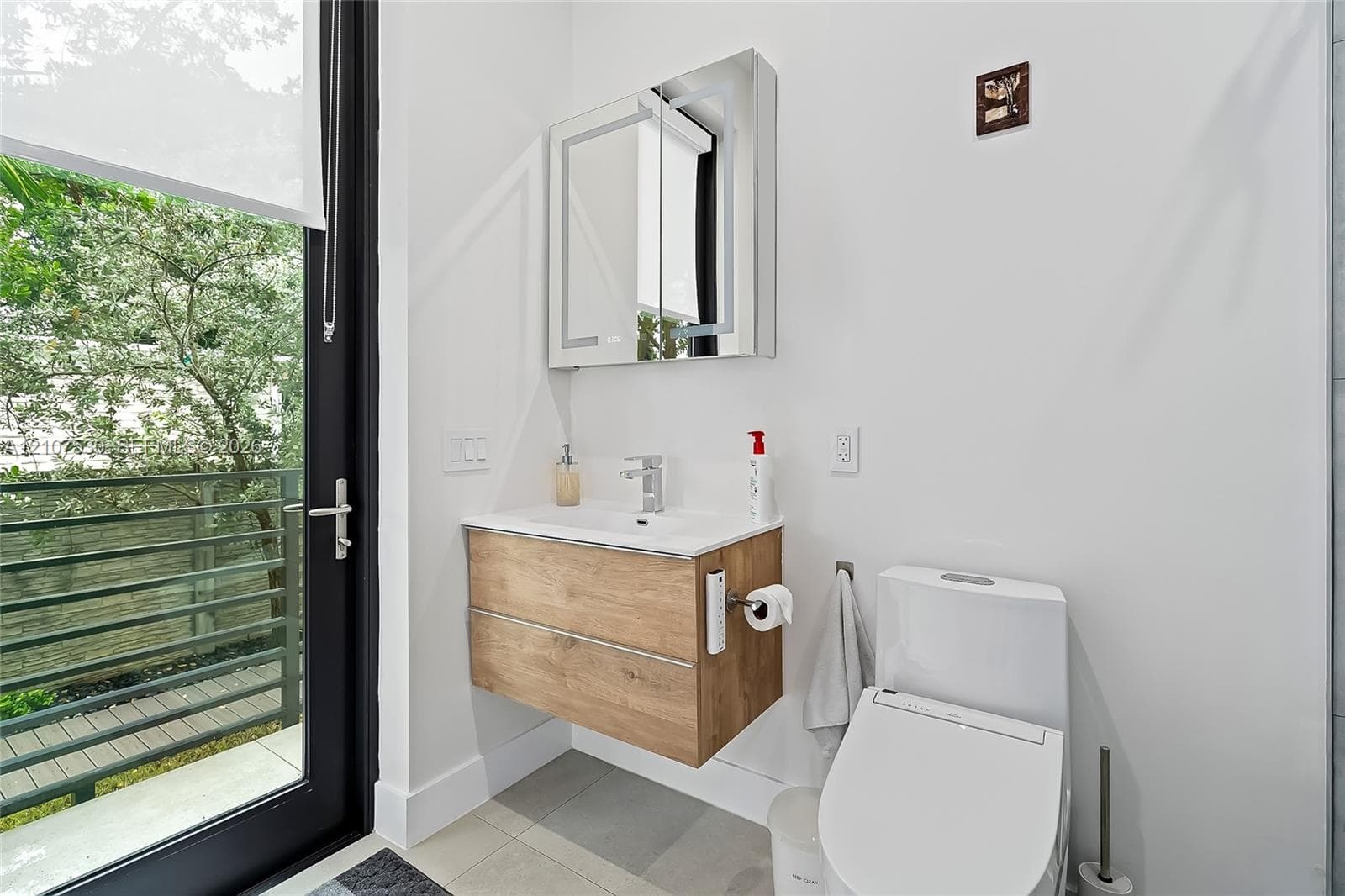 Wall-mounted vanity featuring wood-finish cabinetry and a white integrated sink, paired with a modern mirror-front medicine cabinet, polished chrome faucet, and low-profile toilet