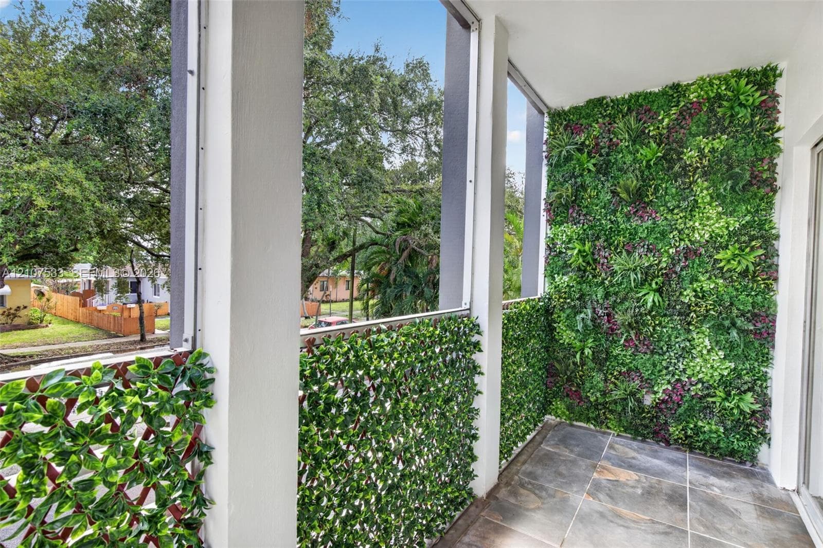 Screened balcony featuring slate-finish tile flooring, vertical garden wall, and decorative greenery privacy screening
