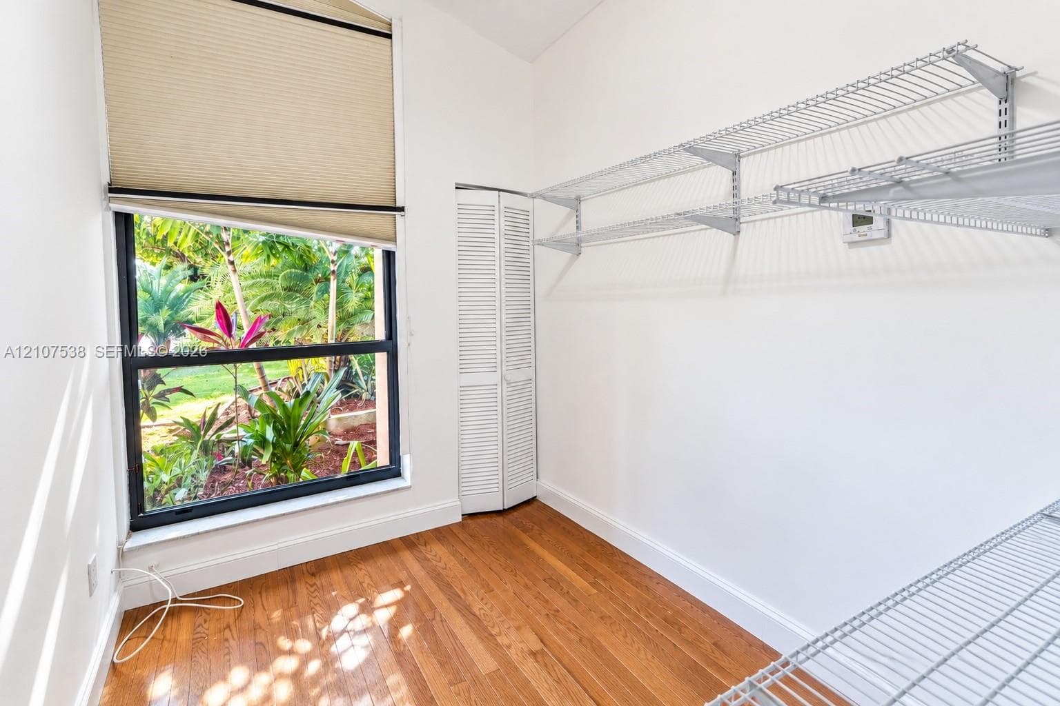 Wood-finish flooring, white louvered-panel closet door, multi-level wire shelving, and floor-to-ceiling window with natural landscape exposure