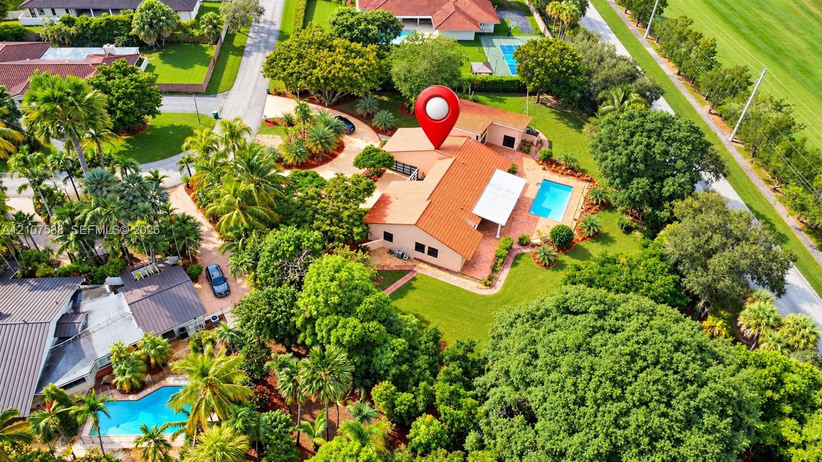 Aerial perspective of a single-story residence featuring a terracotta-tiled roof, an attached pool, a concrete driveway, and established landscaping