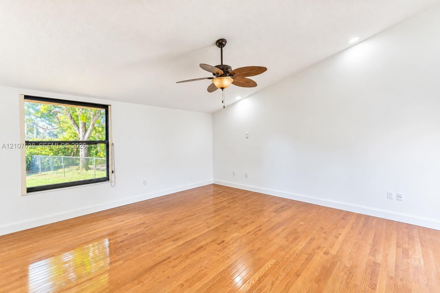 Vaulted ceiling featuring a central five-blade light fixture, wood-finish flooring, and a large single-pane window
