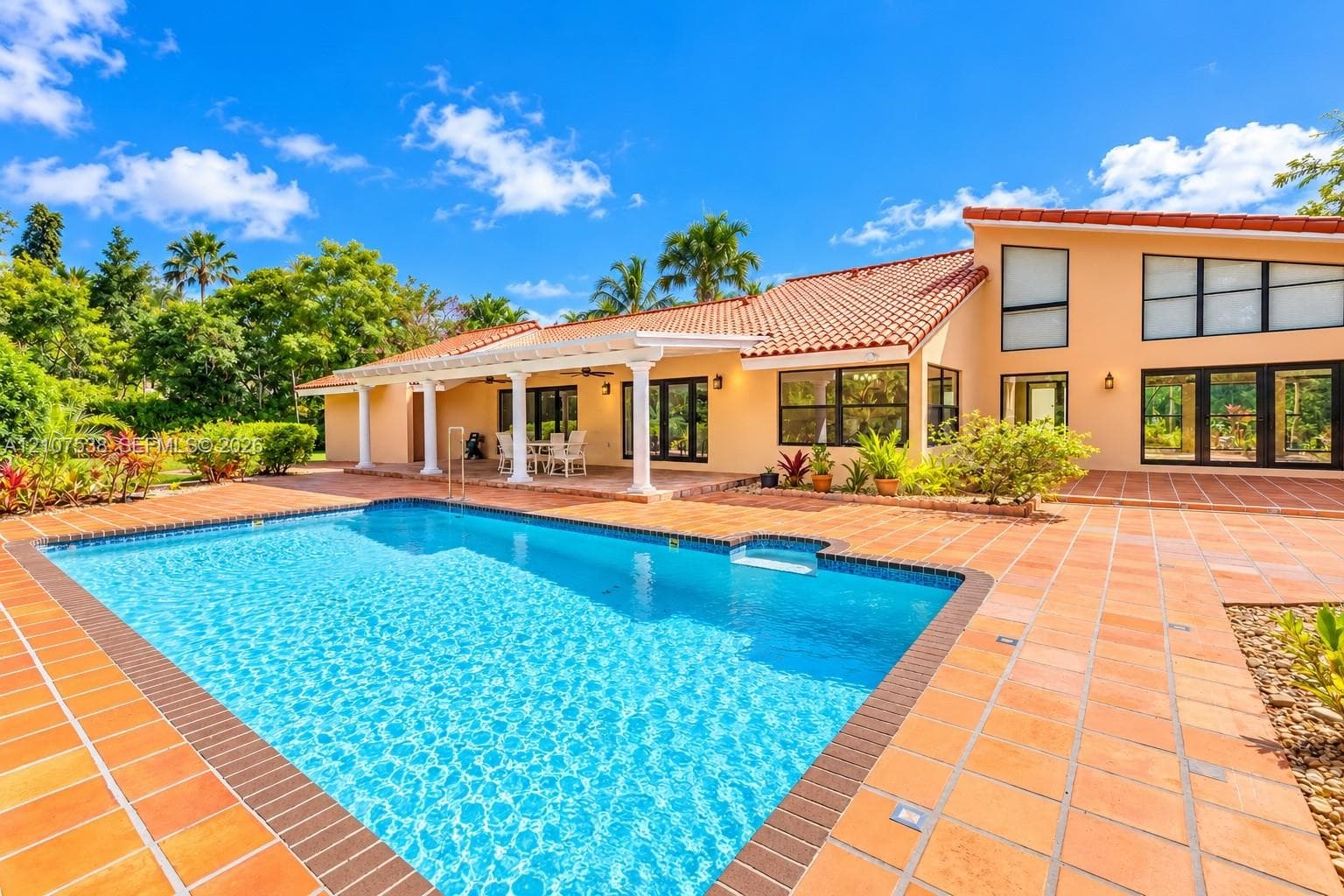 Swimming pool with a tile surround and a covered patio featuring structural columns, terracotta roof tiles, and multi-paned windows