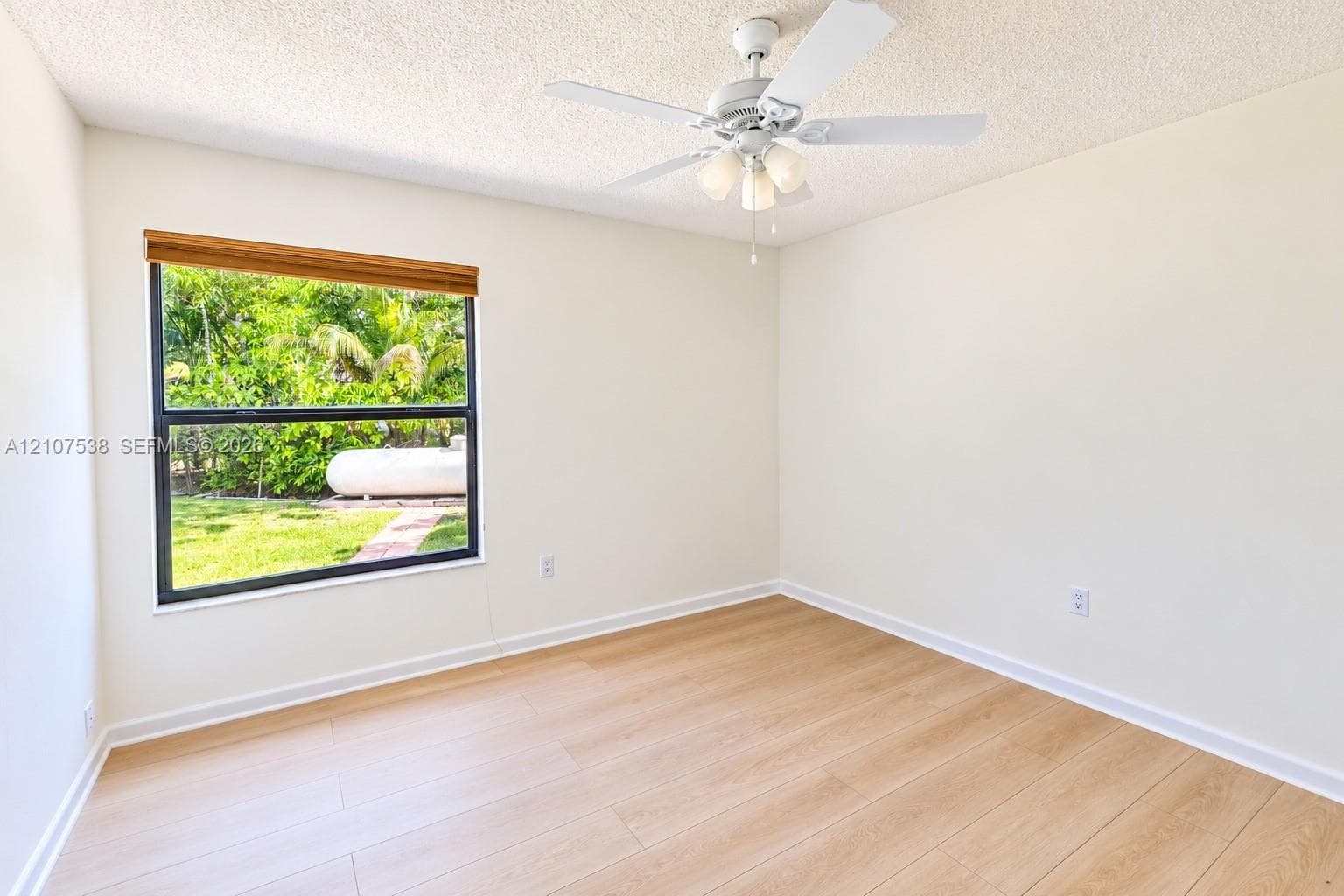 Interior space featuring wood-finish flooring, a ceiling fan with integrated three-light fixture, and a single-pane window with a woven wood blind