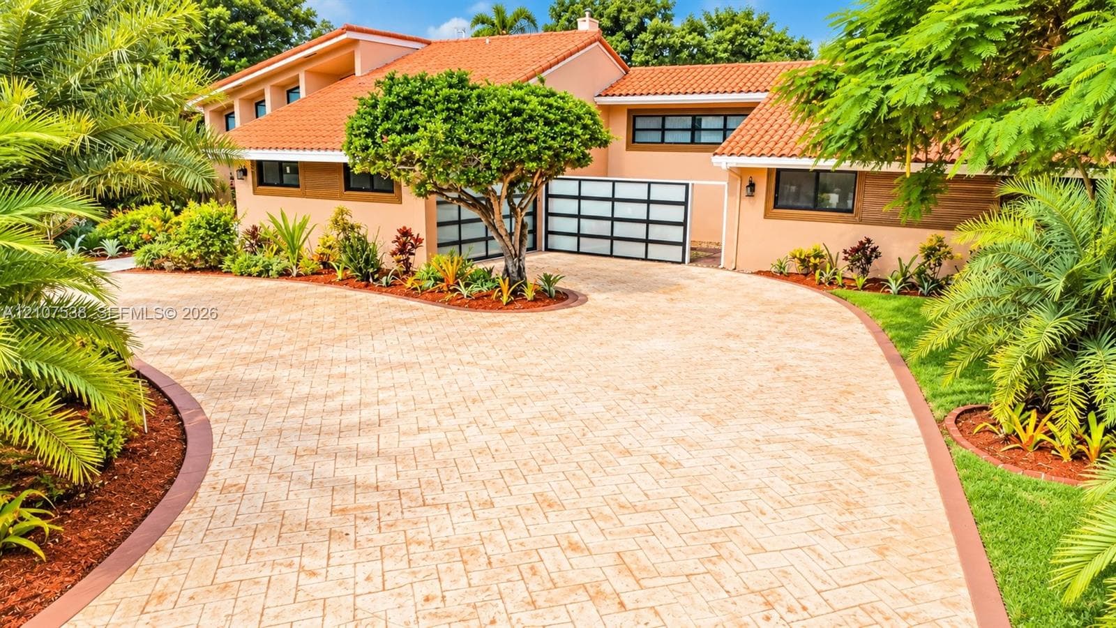 Stucco exterior featuring a terracotta tile roof, paver driveway with decorative border, and modern multi-paneled glass garage doors