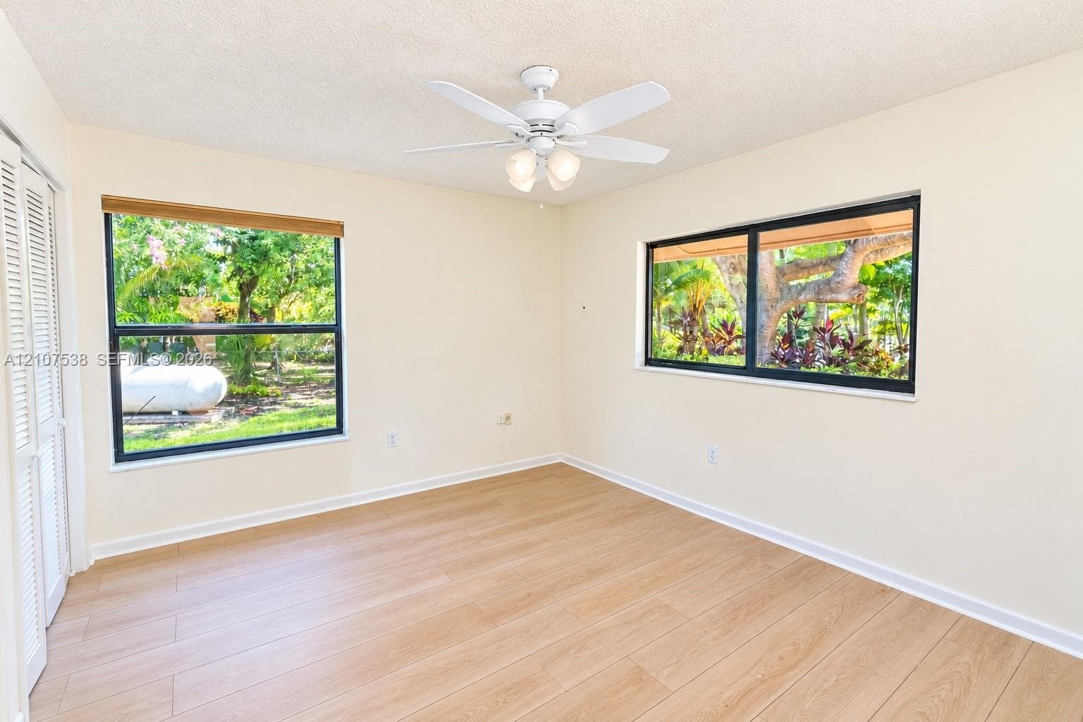 Room featuring wood-finish flooring, dual windows with dark frames, white louvered closet doors, and a ceiling fan with integrated light fixture