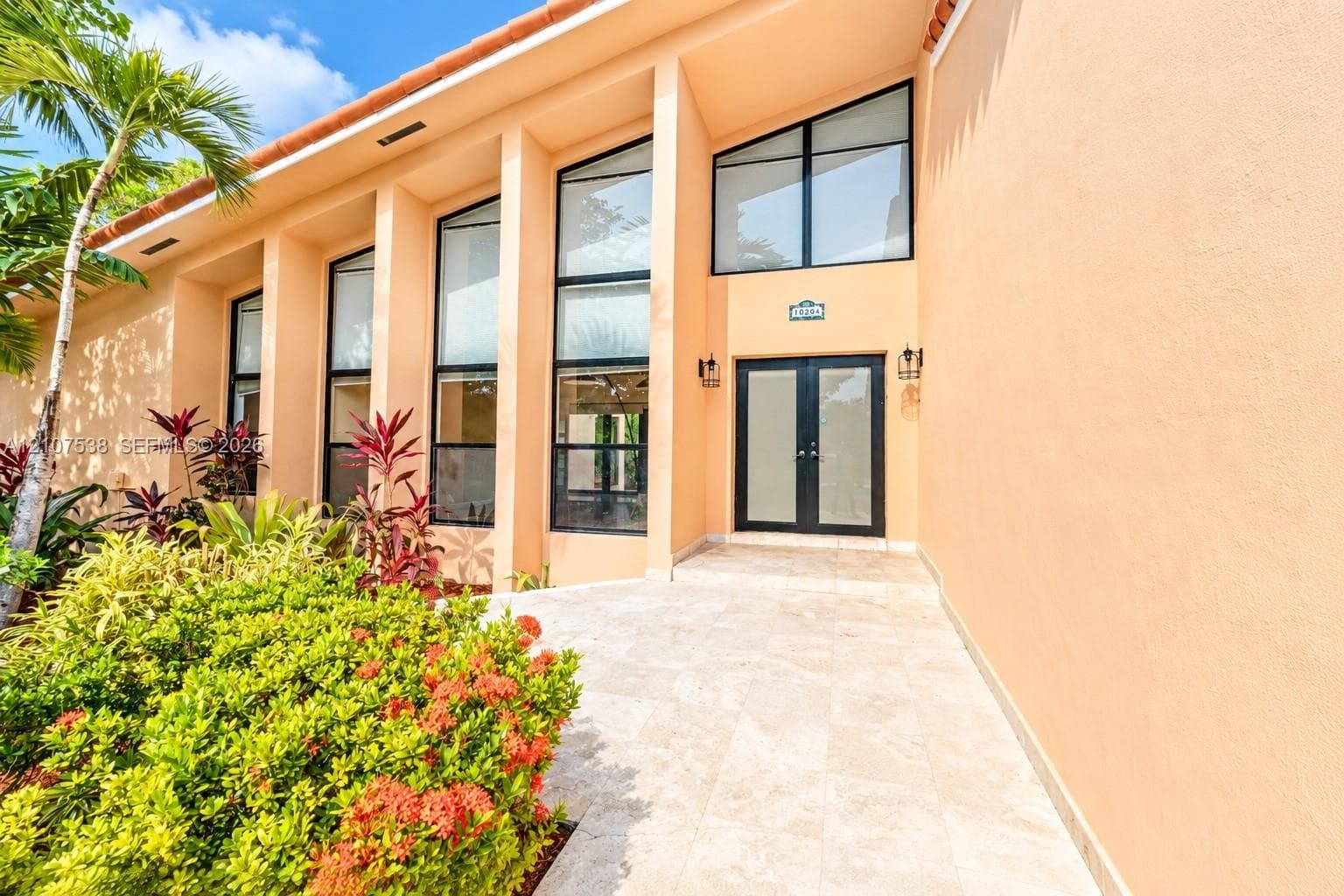 Stucco exterior featuring soaring multi-pane windows, double entry doors, and expansive stone-finish patio flooring