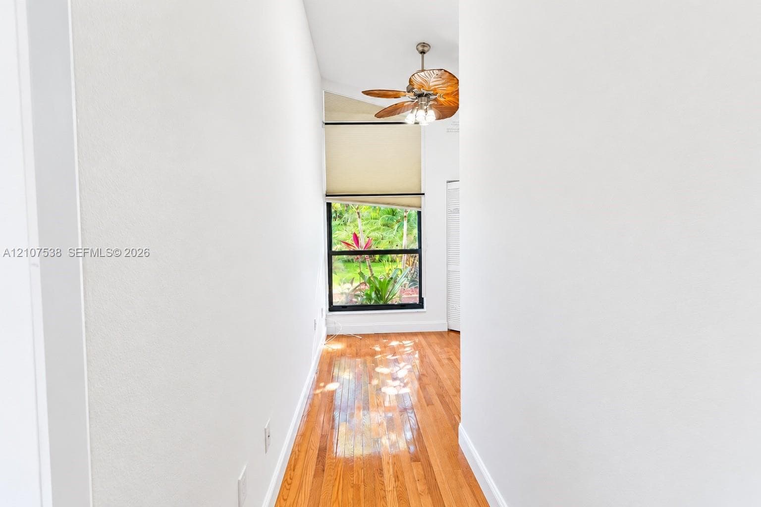 Interior space featuring wood-finish flooring, vaulted ceiling, built-in paddle ceiling fan with integrated lighting, and a window with black trim