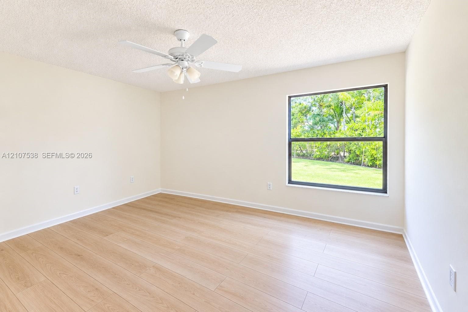 Neutral-toned interior featuring wood-finish flooring, a white ceiling fan with integrated lighting, and a large single-pane window