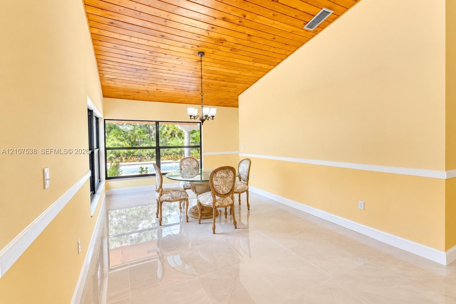 Vaulted wood-plank ceiling, large-format tile flooring, chair rail molding, and a suspended multi-light chandelier