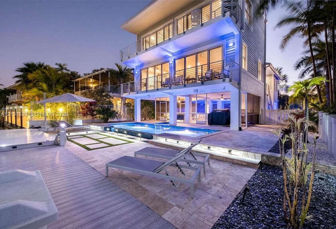 Multi-story coastal residence featuring a stone-paved pool deck, elevated balconies with metal railings, a swimming pool with integrated lighting, and tiered hardscaping