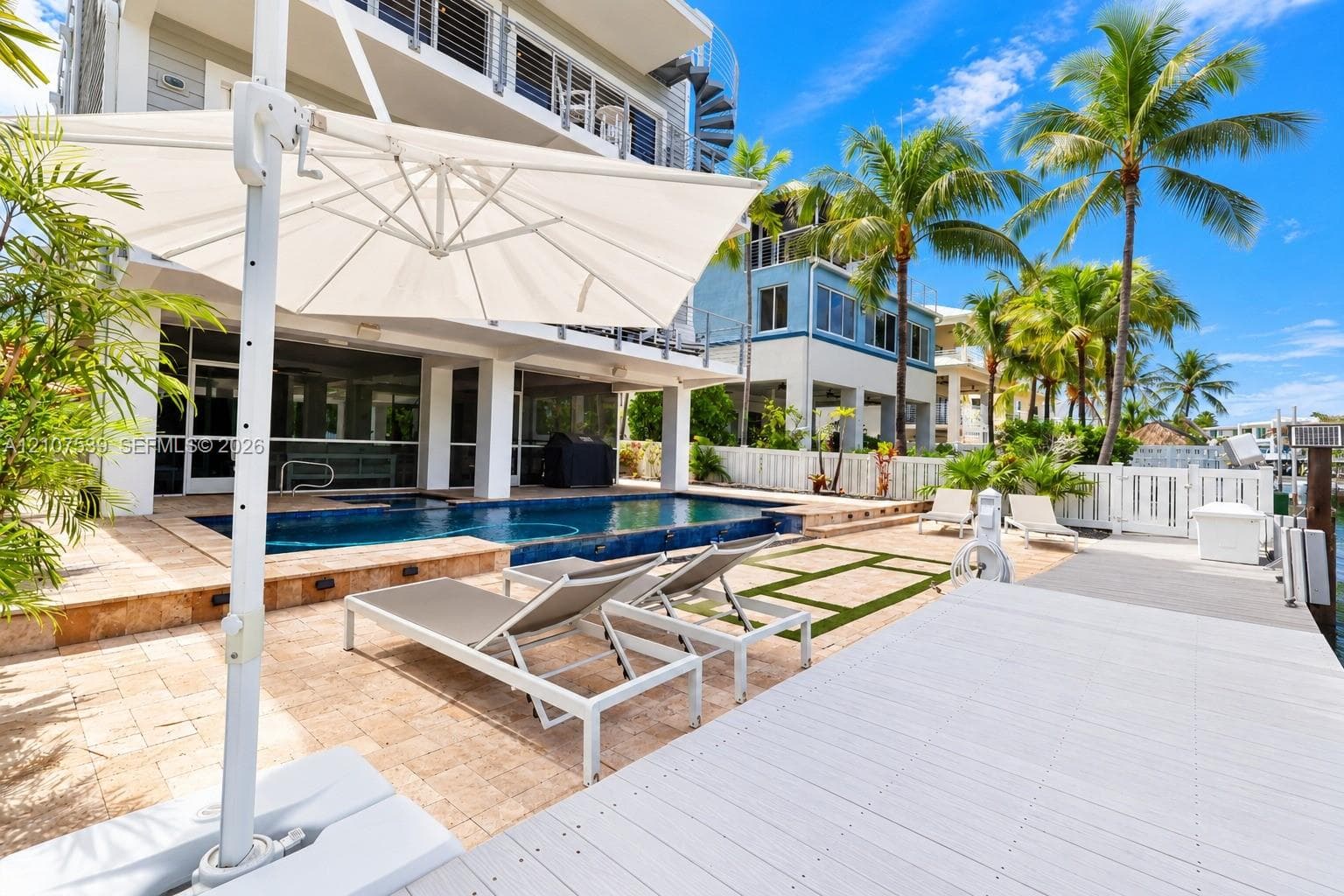 Outdoor living area featuring a swimming pool, stone-finish paver patio, composite dock, and a spiral exterior staircase