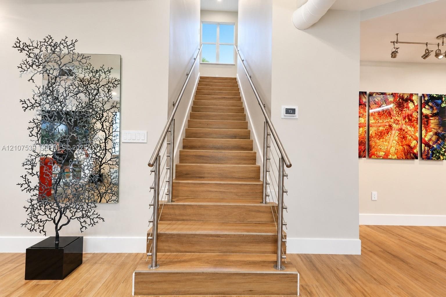 Staircase featuring wood-finish treads, stainless steel cable railings, and a metal handrail