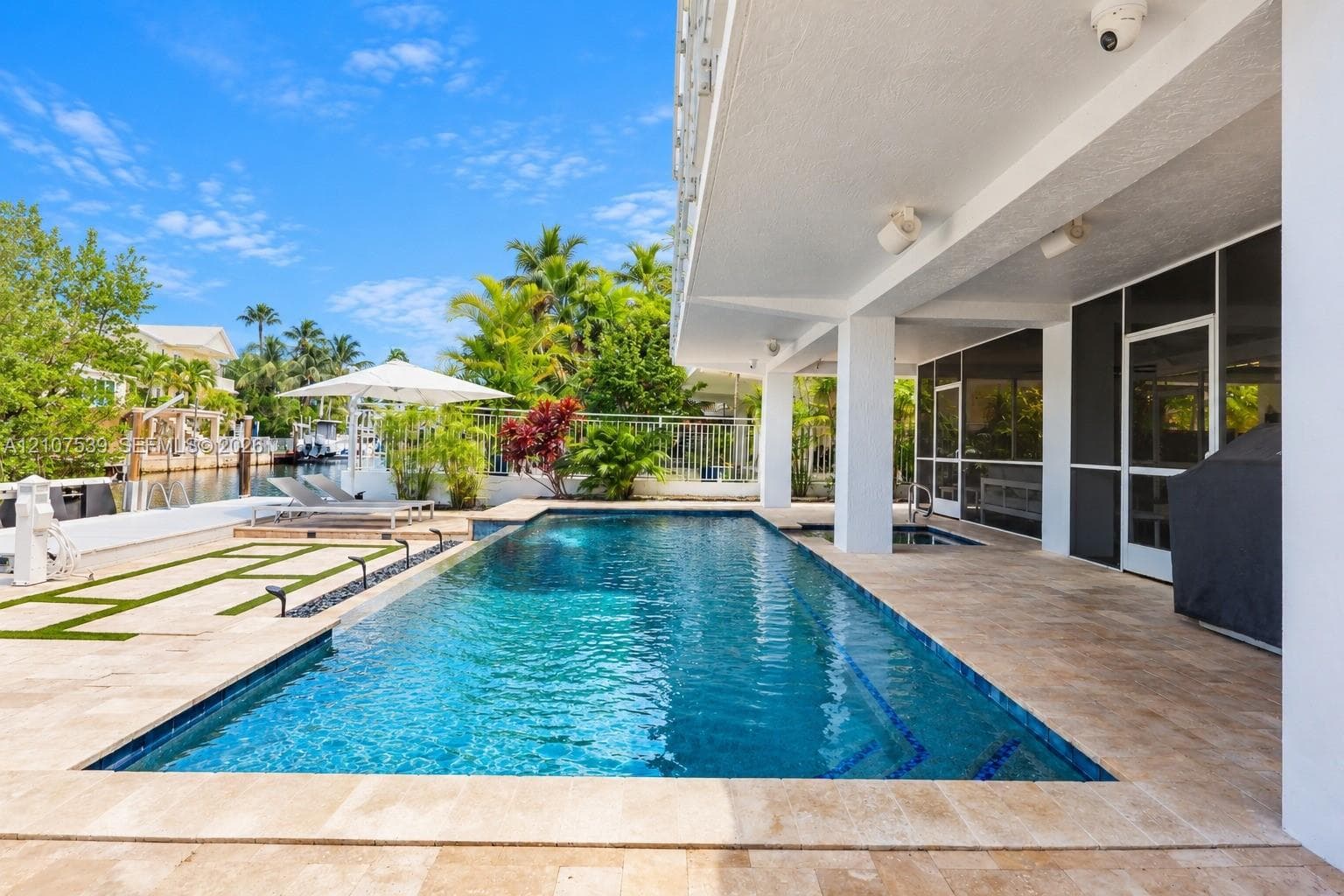 In-ground pool with tiled waterline and stone decking, covered patio, integrated spa, and waterfront bulkhead