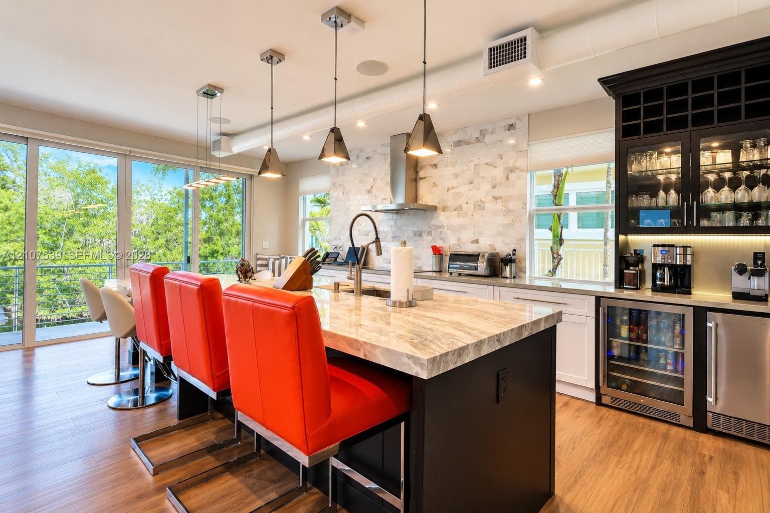 Kitchen featuring a spacious island with stone-finish countertops, custom cabinetry with integrated wine storage, a stainless steel range hood, stone-style backsplash, and wood-finish flooring