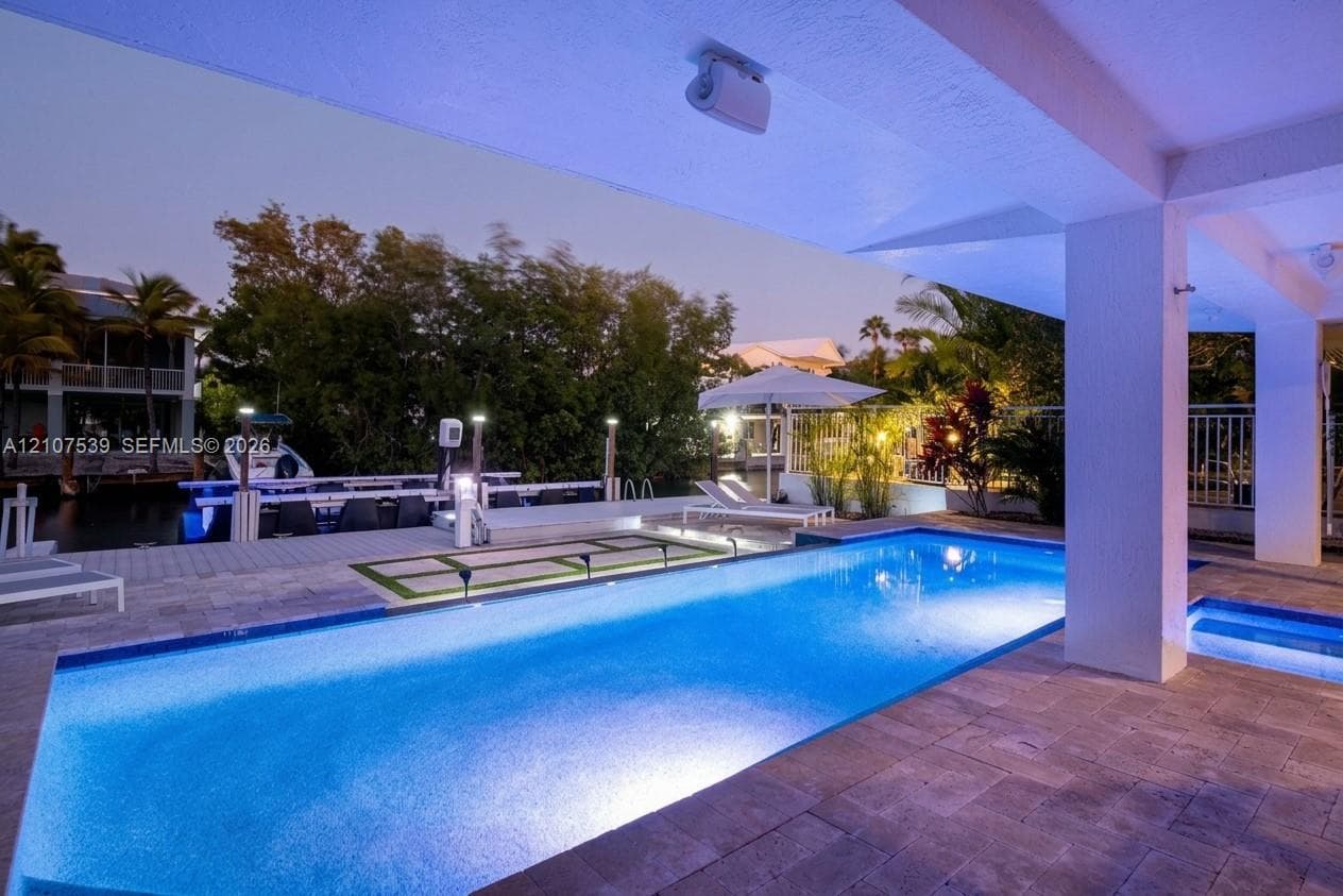 Covered patio featuring stone paver flooring, a private swimming pool with an integrated spa, and a boat dock with direct water access