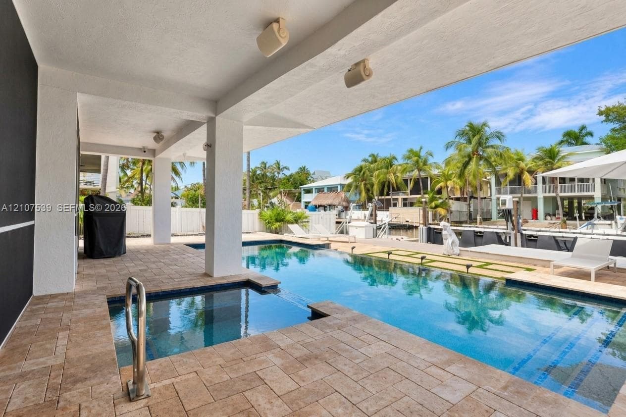 Covered lanai with stone-paver decking, swimming pool featuring an integrated spa, and concrete bulkhead leading to a waterway