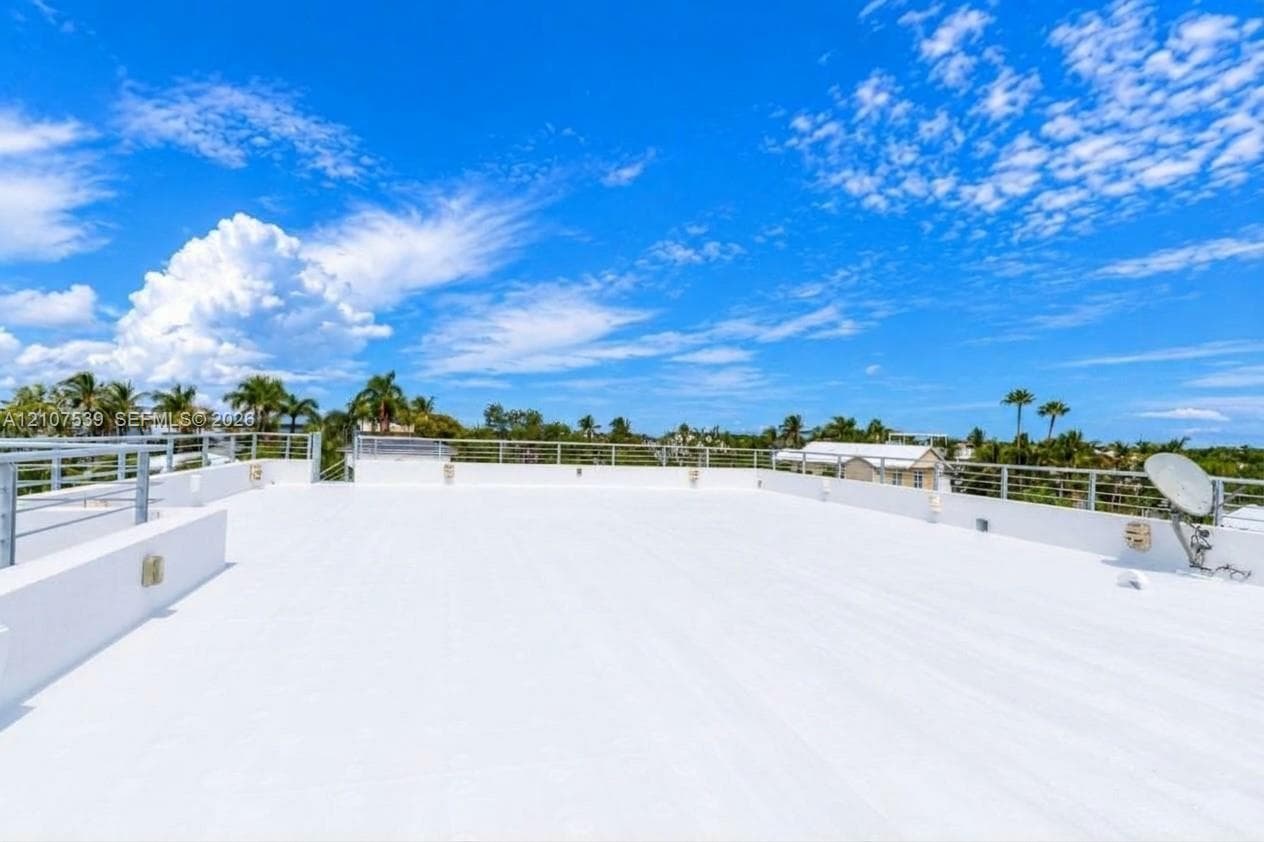 Expansive rooftop terrace featuring a flat, white deck surface and a metallic horizontal-bar railing