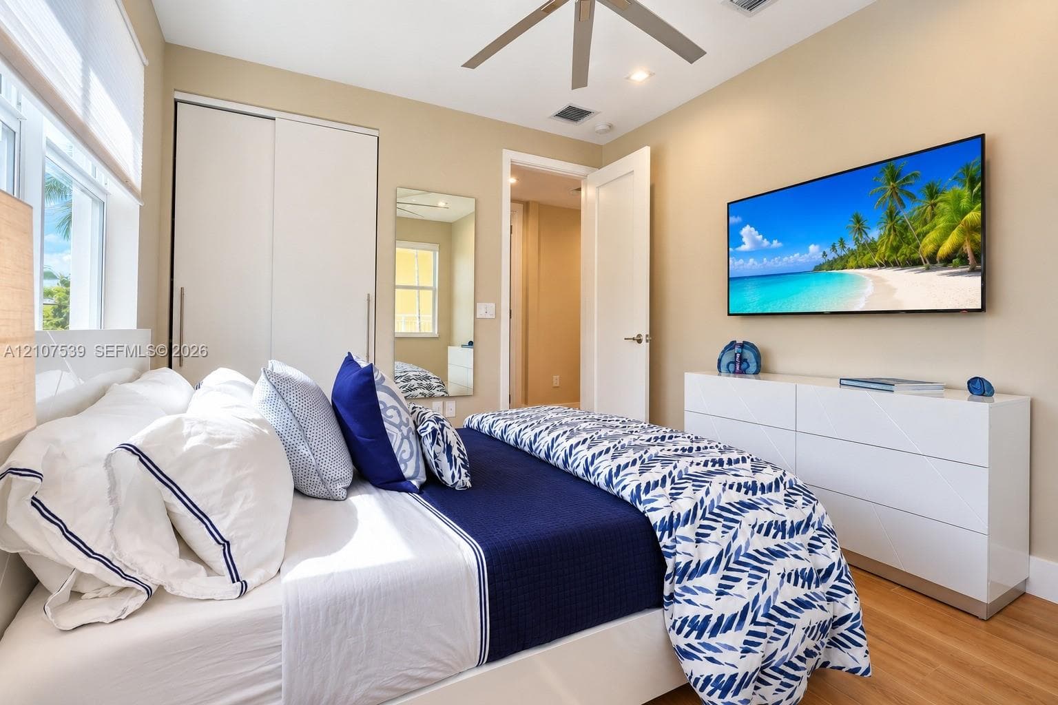 Wood-finish flooring, ceiling fan, sliding-door closet, wall-mounted mirror, and multi-panel interior door