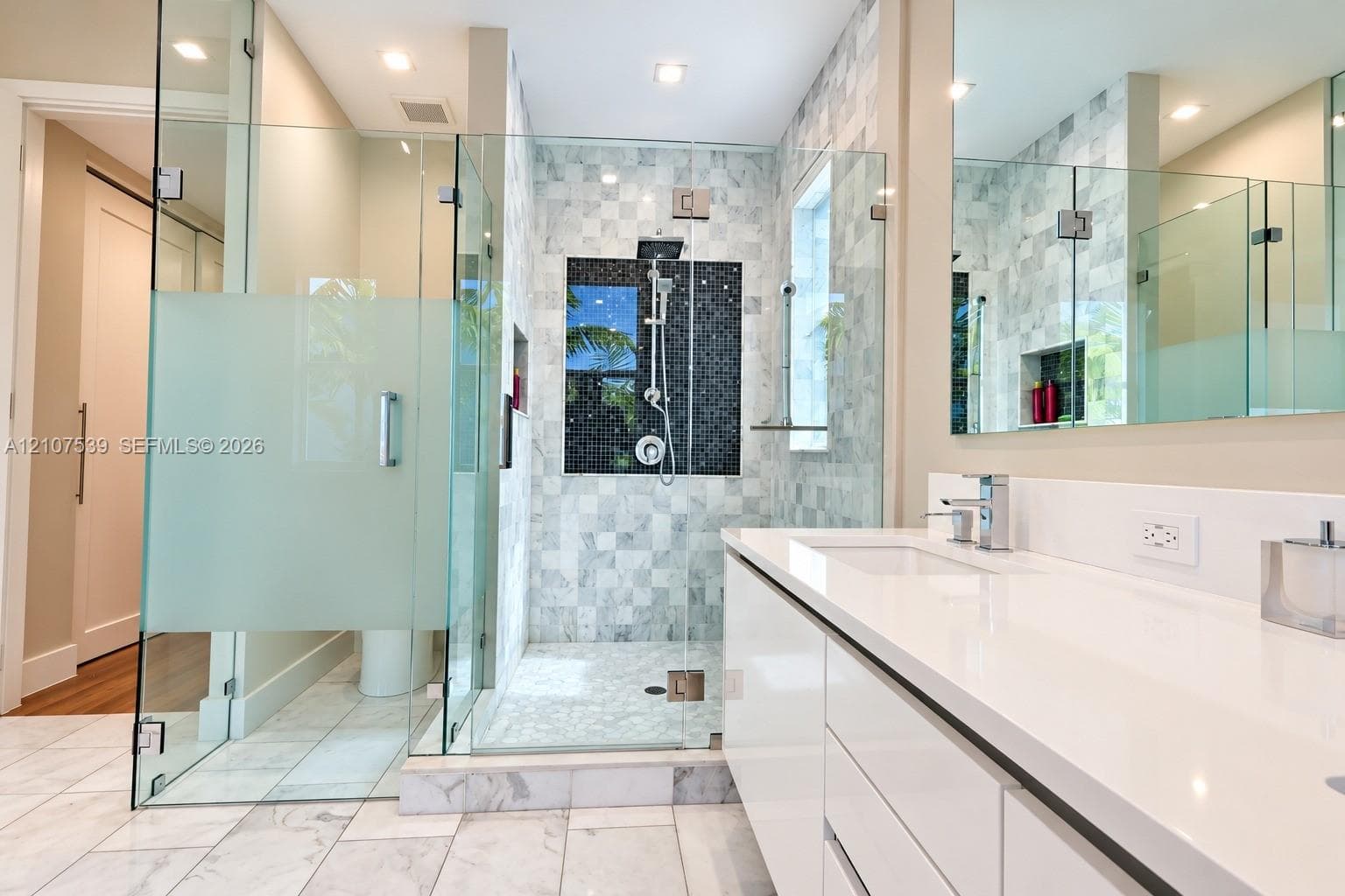 Bathroom featuring a white flat-panel vanity with a stone countertop, a glass-enclosed walk-in shower with tiled walls and a built-in recessed niche, and polished stone flooring