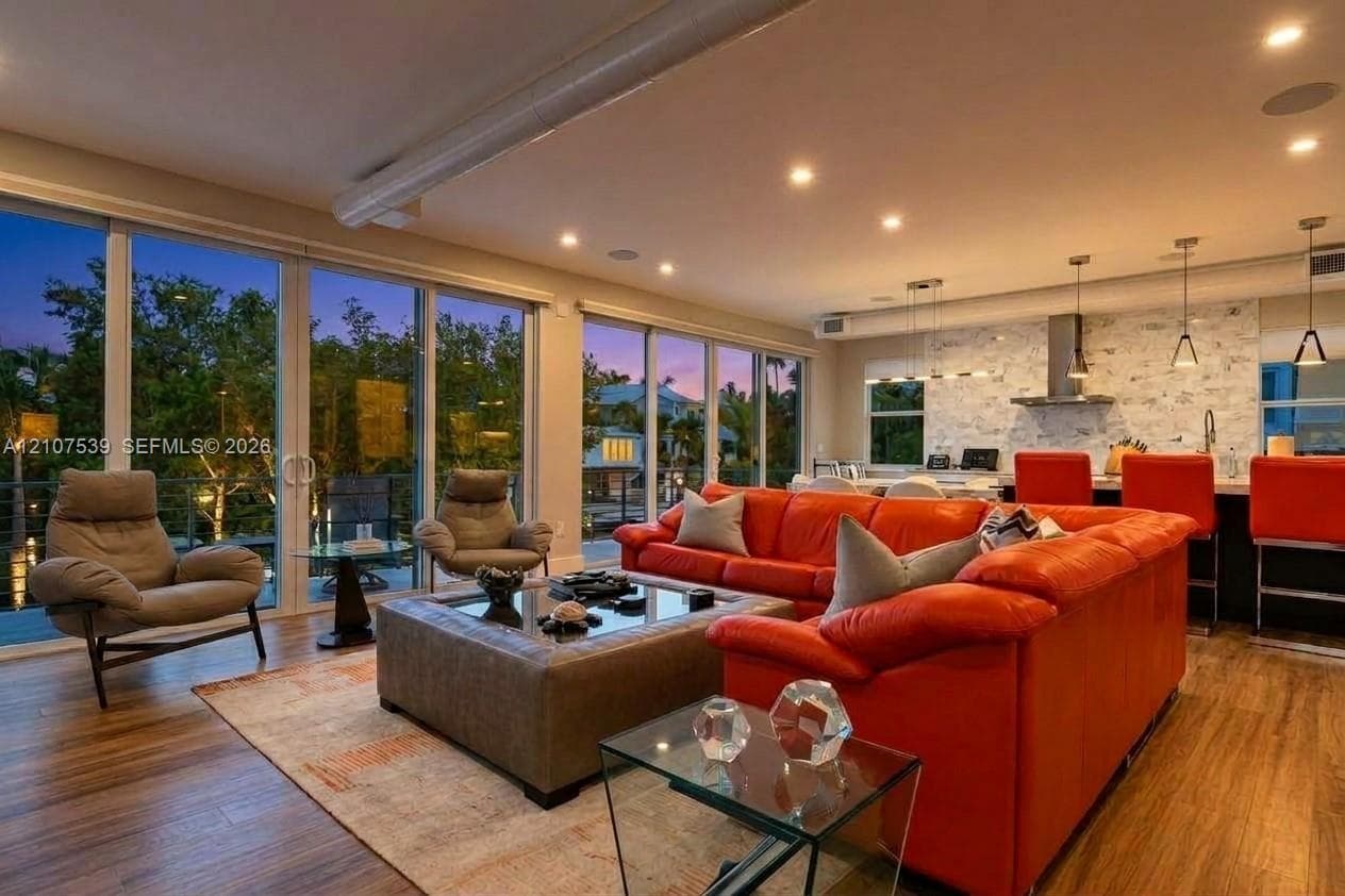 Open-concept living space featuring expansive floor-to-ceiling glass doors, wood-finish flooring, recessed lighting, and kitchen backsplash with stone-finish cladding