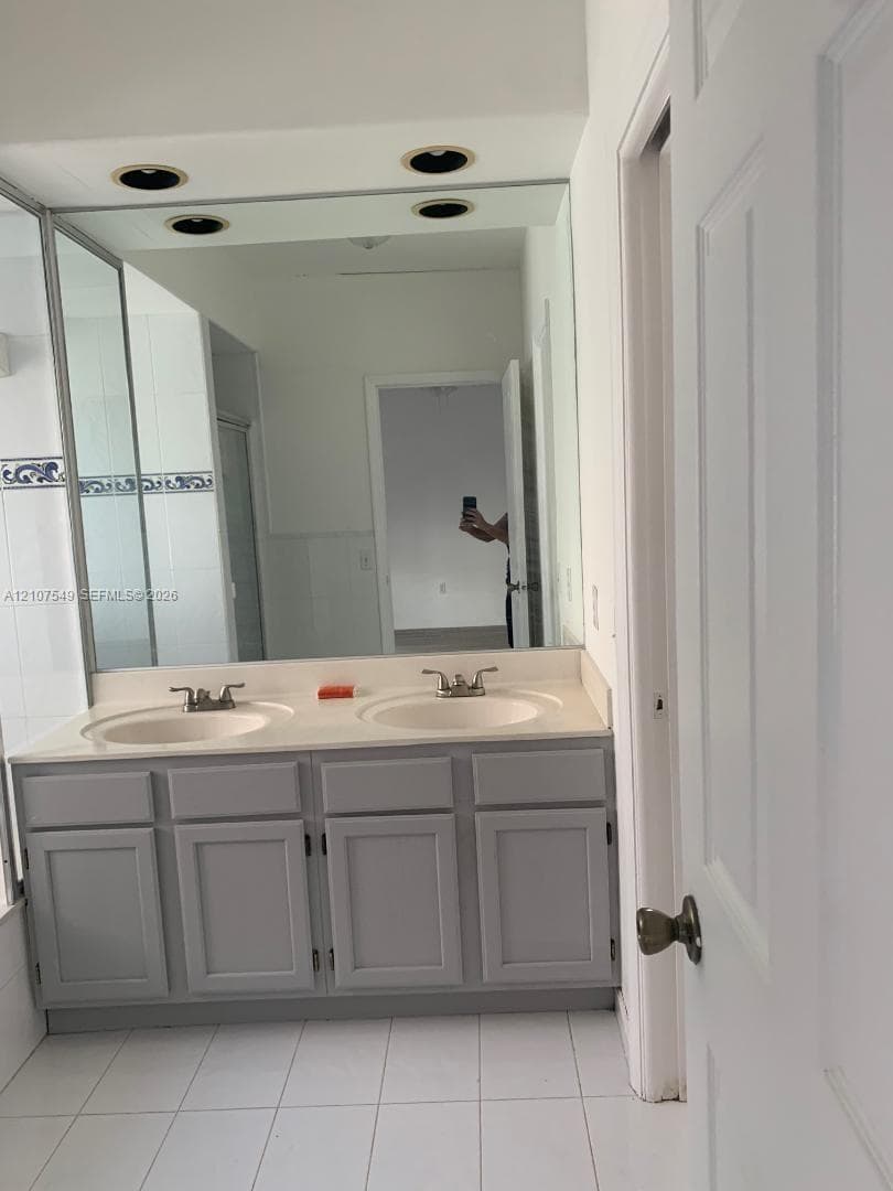 Dual-sink vanity with gray shaker-style cabinetry, solid-surface countertop, integrated basins, and large wall-to-wall mirror with recessed lighting