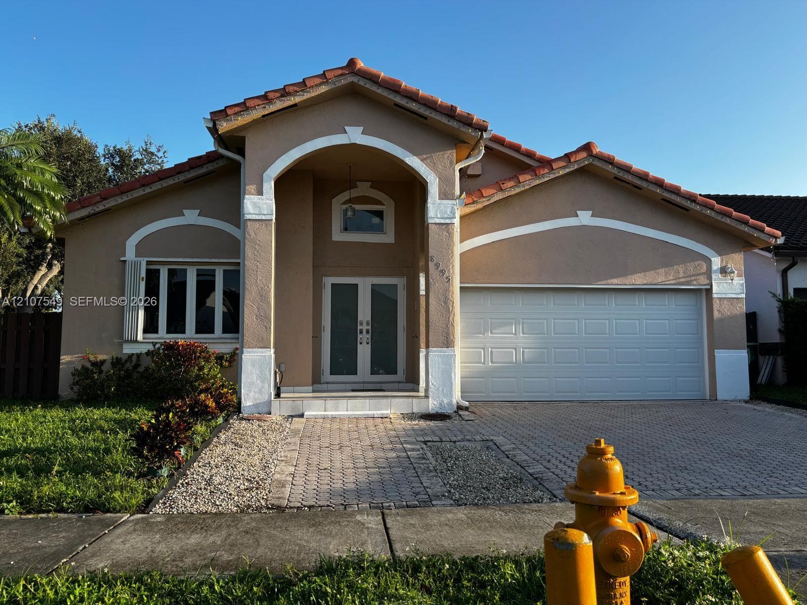 Stucco exterior with a tiled roof, arched entryway, double-door entrance, and a paved driveway