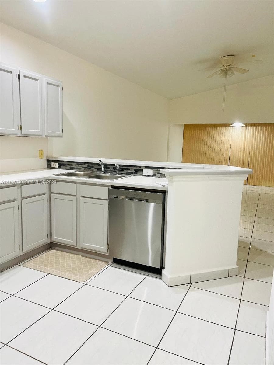 Kitchen featuring white shaker-style cabinetry, stainless steel dishwasher, dual-basin stainless steel sink, tiled backsplash, and white tile flooring