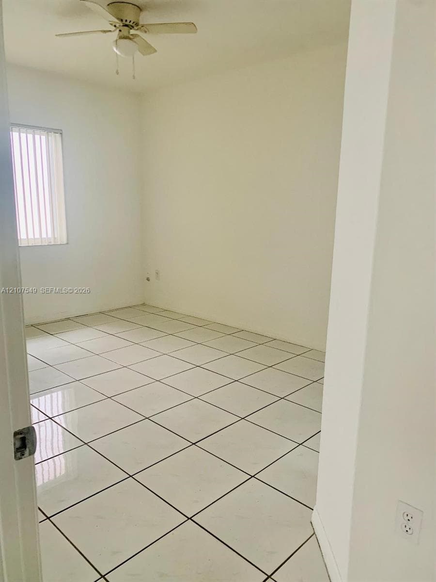 Room featuring large-format ceramic tile flooring, neutral wall finishes, a ceiling fan with integrated lighting, and vertical blinds on the window