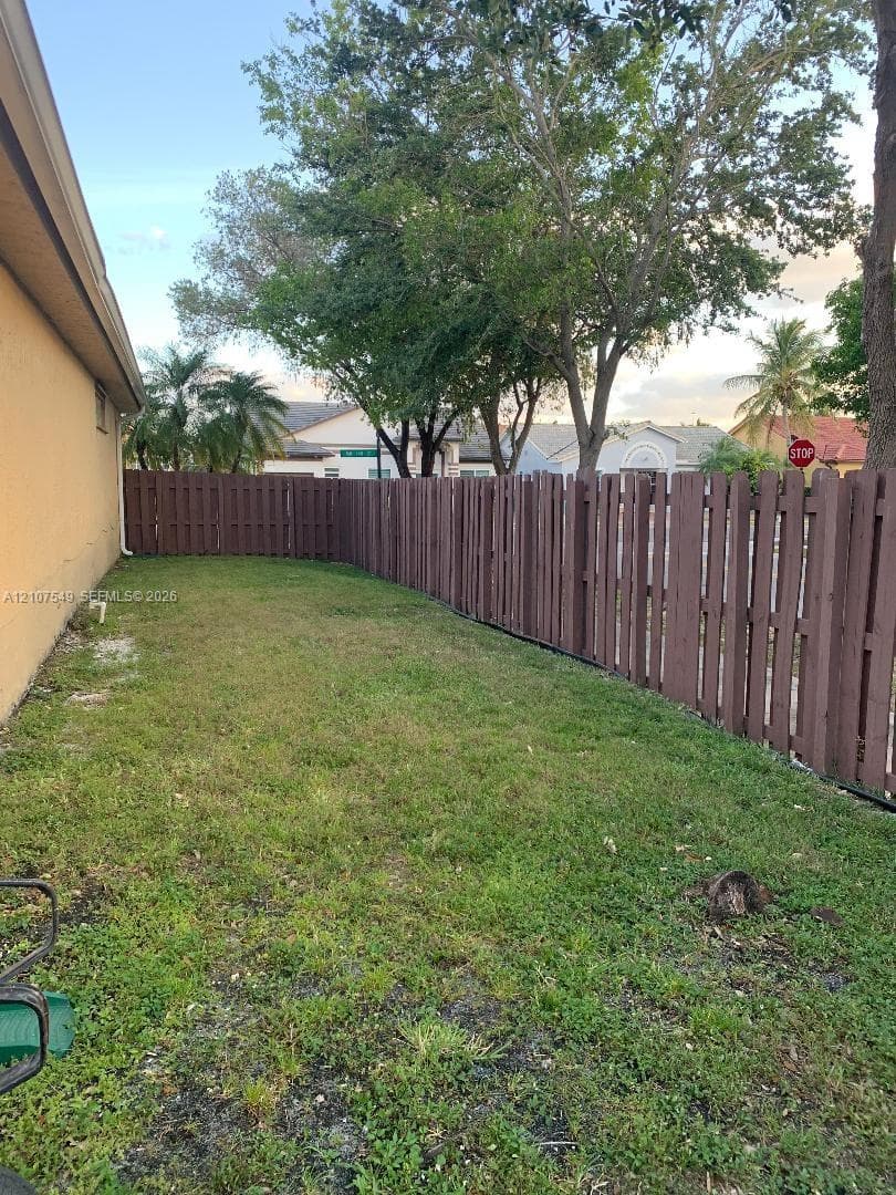 Side yard area featuring a grass lawn enclosed by a tall stained-wood fence and mature trees