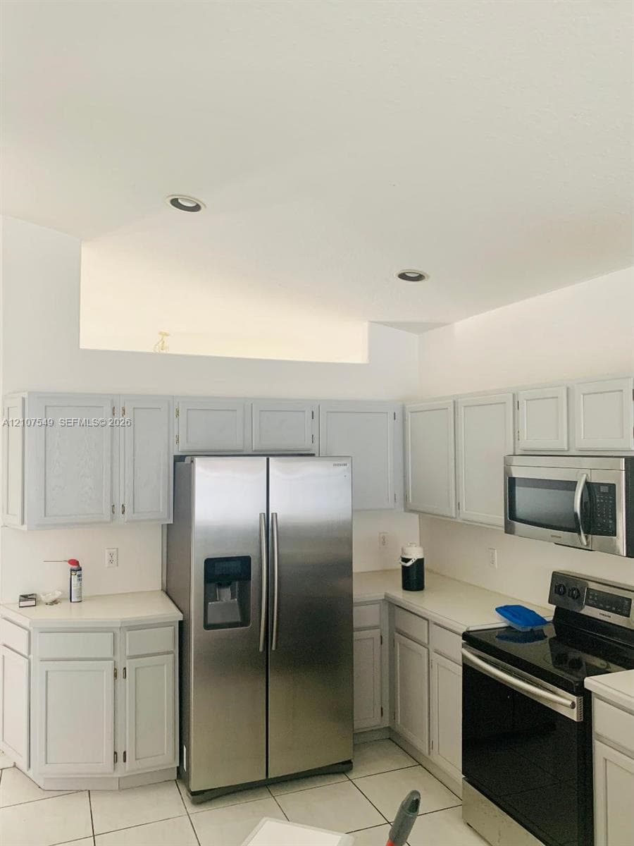 Kitchen featuring light-toned cabinetry, solid-surface countertops, stainless steel side-by-side refrigerator, built-in microwave, and recessed ceiling lighting