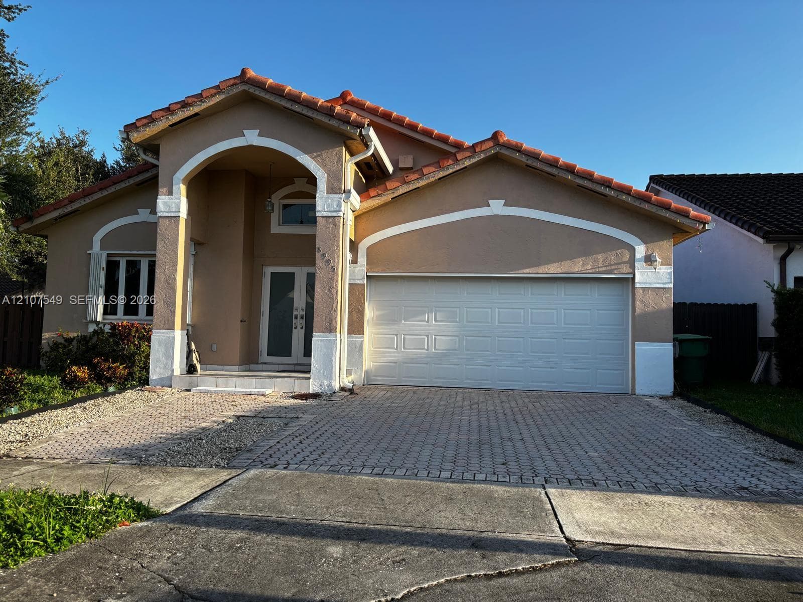 Stucco exterior featuring arched architectural detailing, tile roof, dual-glass panel entry door, and paver driveway