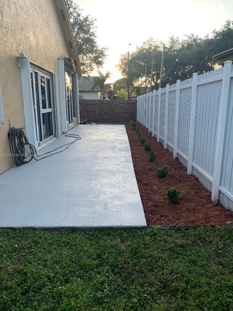 Concrete patio featuring a white vinyl privacy fence and a mulch-lined garden border with shrubbery