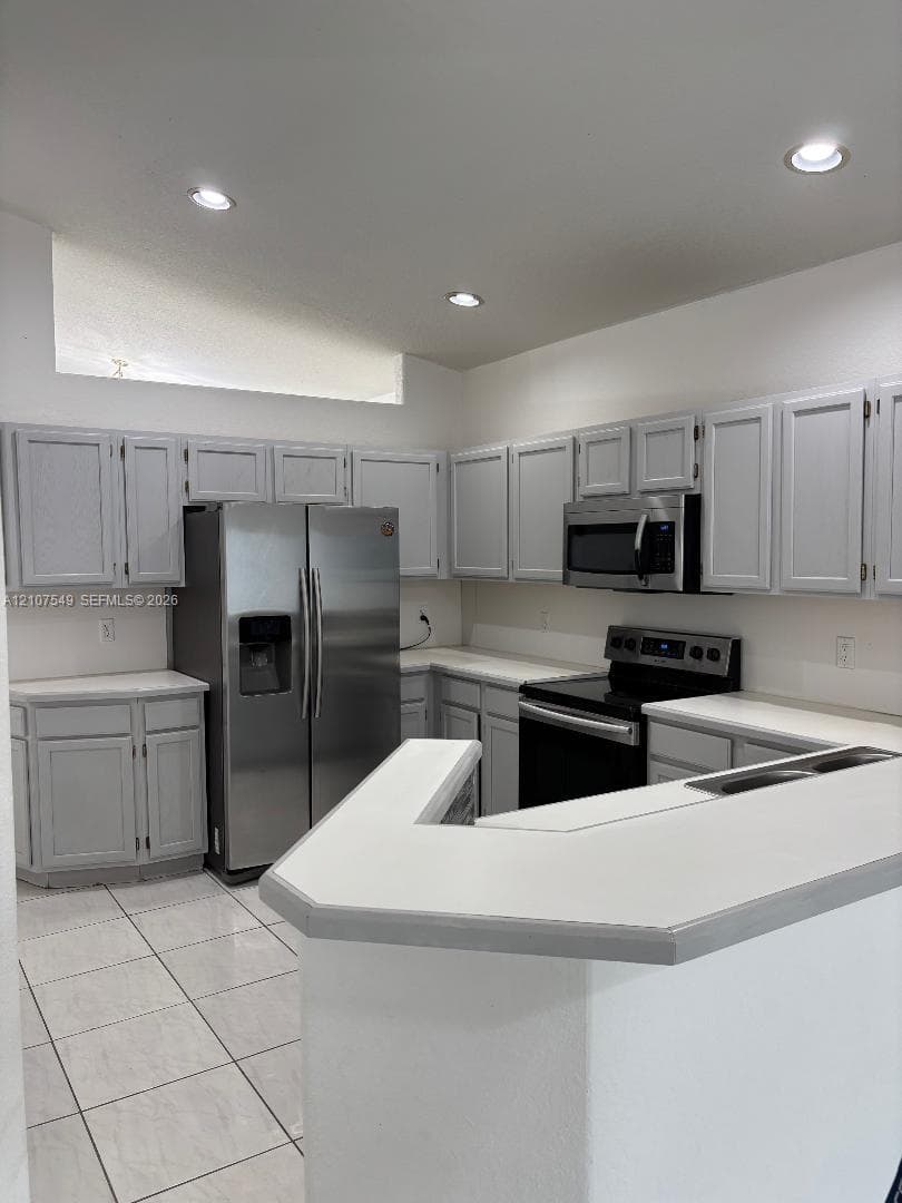Kitchen featuring light-toned cabinetry, solid surface countertops, stainless steel appliances, a peninsula counter, and tiled flooring
