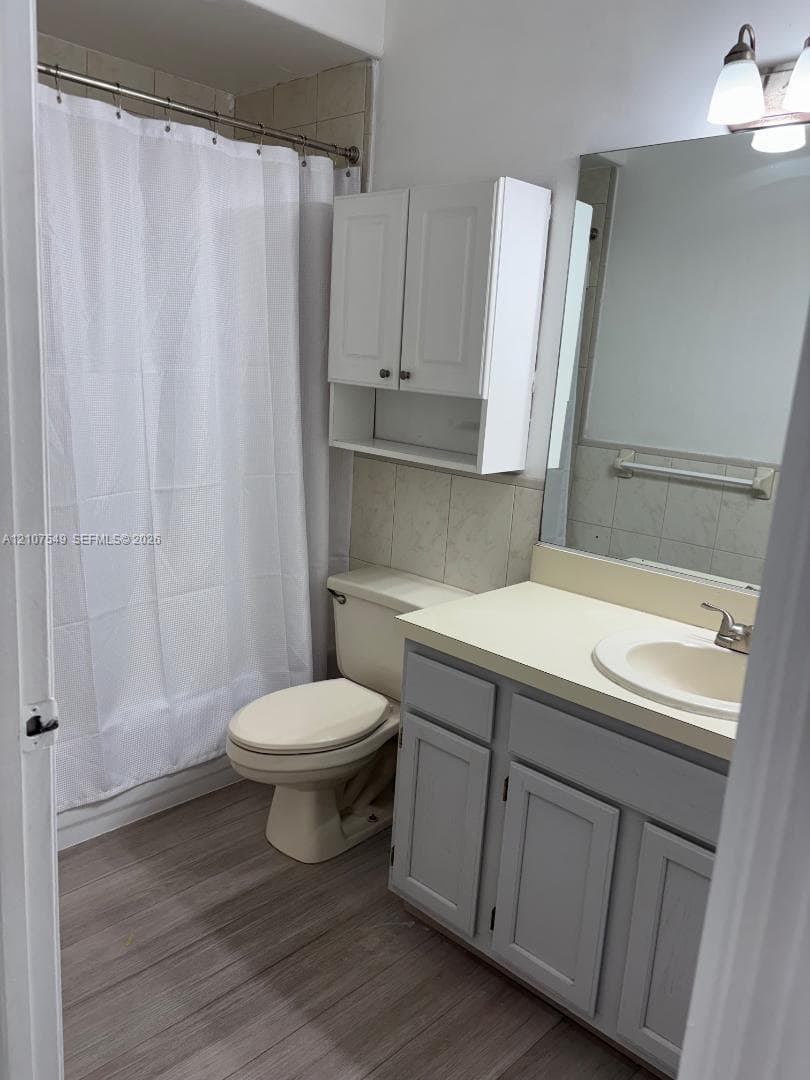 Bathroom featuring wood-finish flooring, a vanity cabinet with a neutral countertop and integrated sink, wall-mounted storage cabinetry, a large vanity mirror, and a tub-shower combination with tile surround